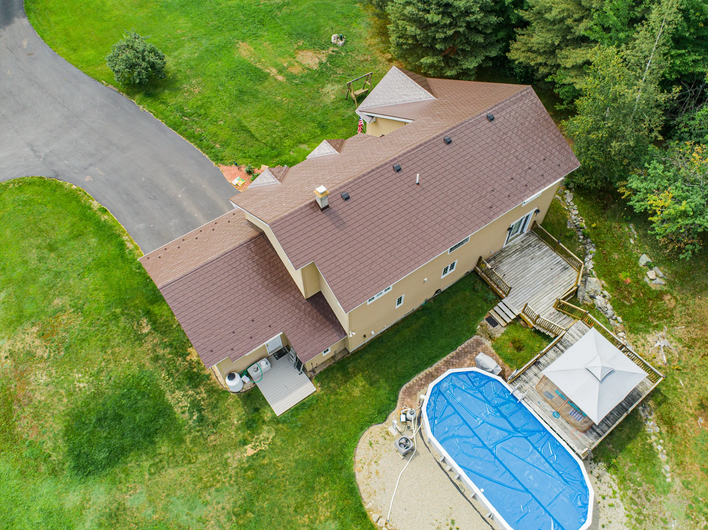 Colonial Brown Interlock Slate aluminum roof on a colonial home with a brown roof among tall trees, Milan, New Hampshire