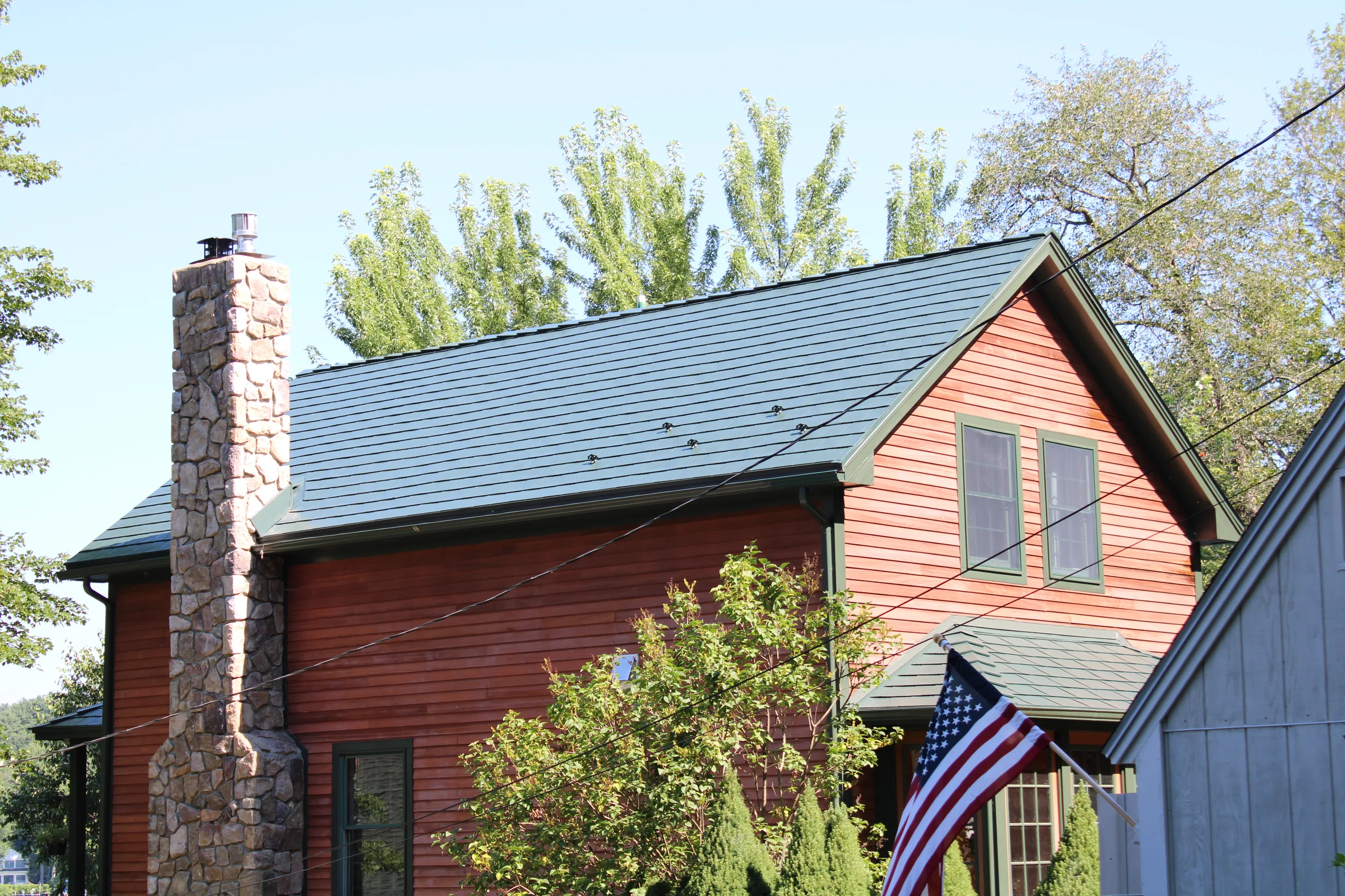 Hunter Green Interlock Slate aluminum roof on a red colonial home with dormers among tall trees, Pelham, New Hampshire