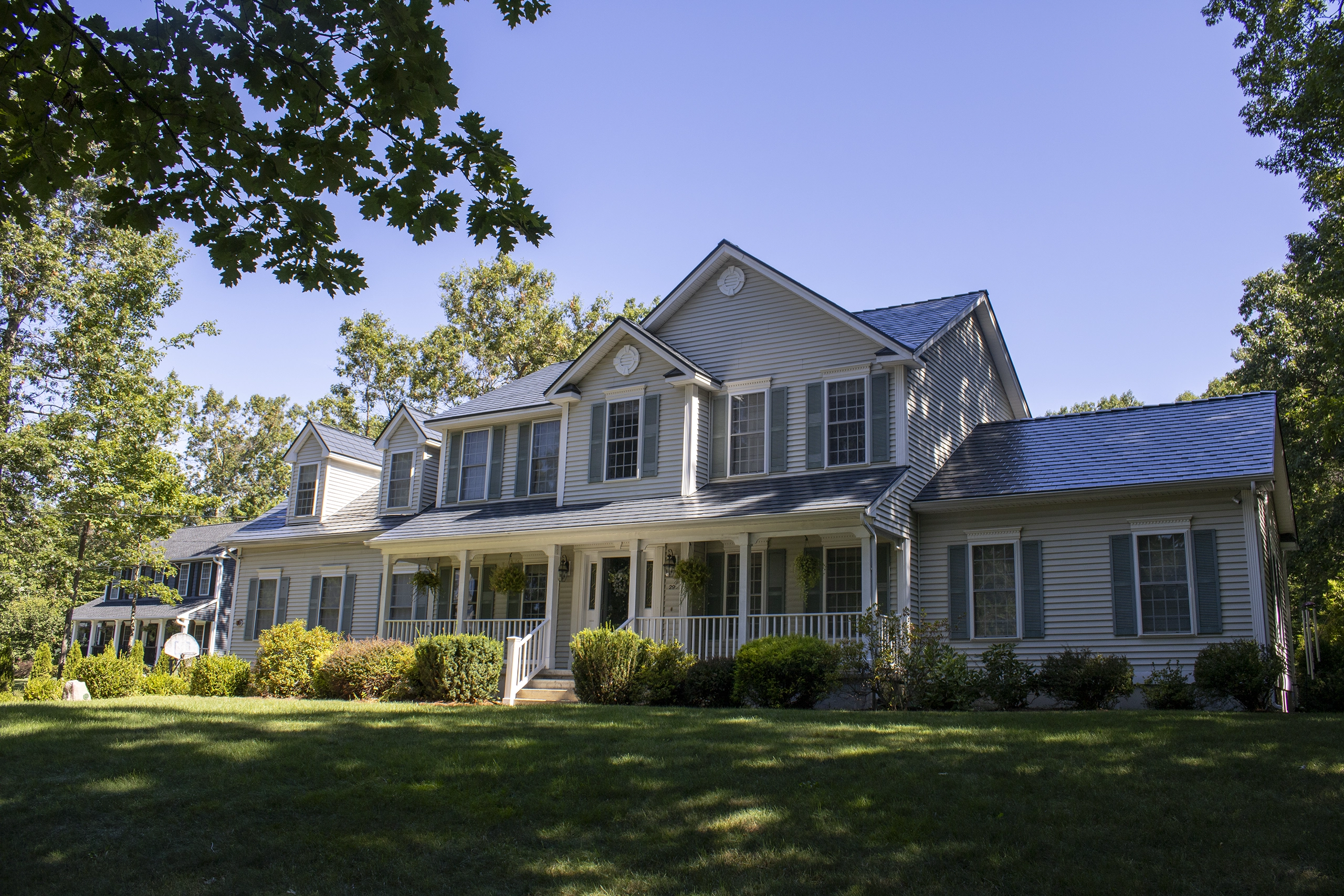 Two-story Colonial home in Hooksett, NH with Interlock deep charcoal aluminum slate metal roofing, multiple dormers, and a full-width covered front porch.