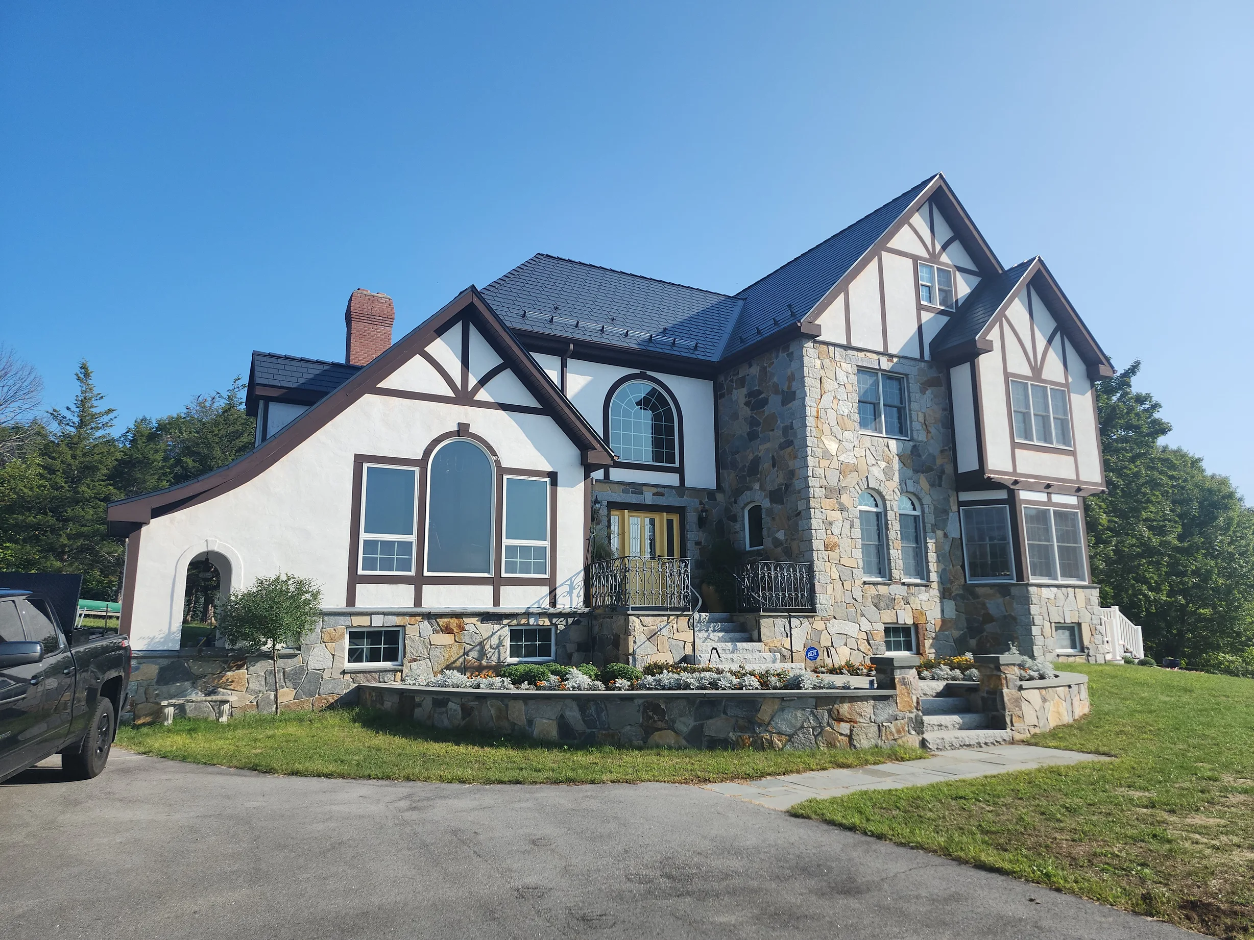 Deep Charcoal Interlock Slate aluminum roof on a two-storey Tudor home with dormers among tall trees, Madbury, New Hampshire