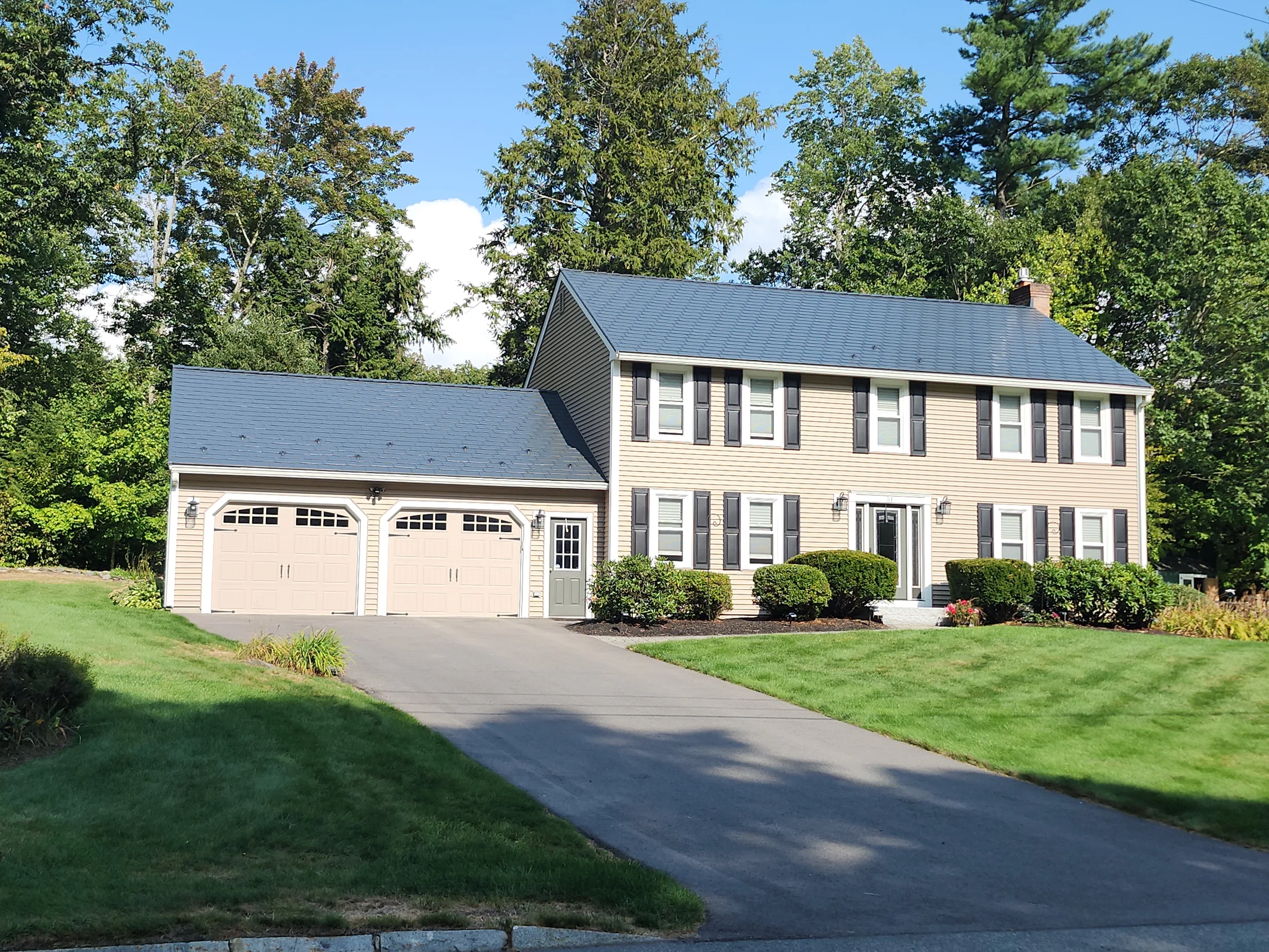 Deep Charcoal Interlock Slate aluminum roof on a tan two-storey home with dormers among tall green trees, Nashua, New Hampshire