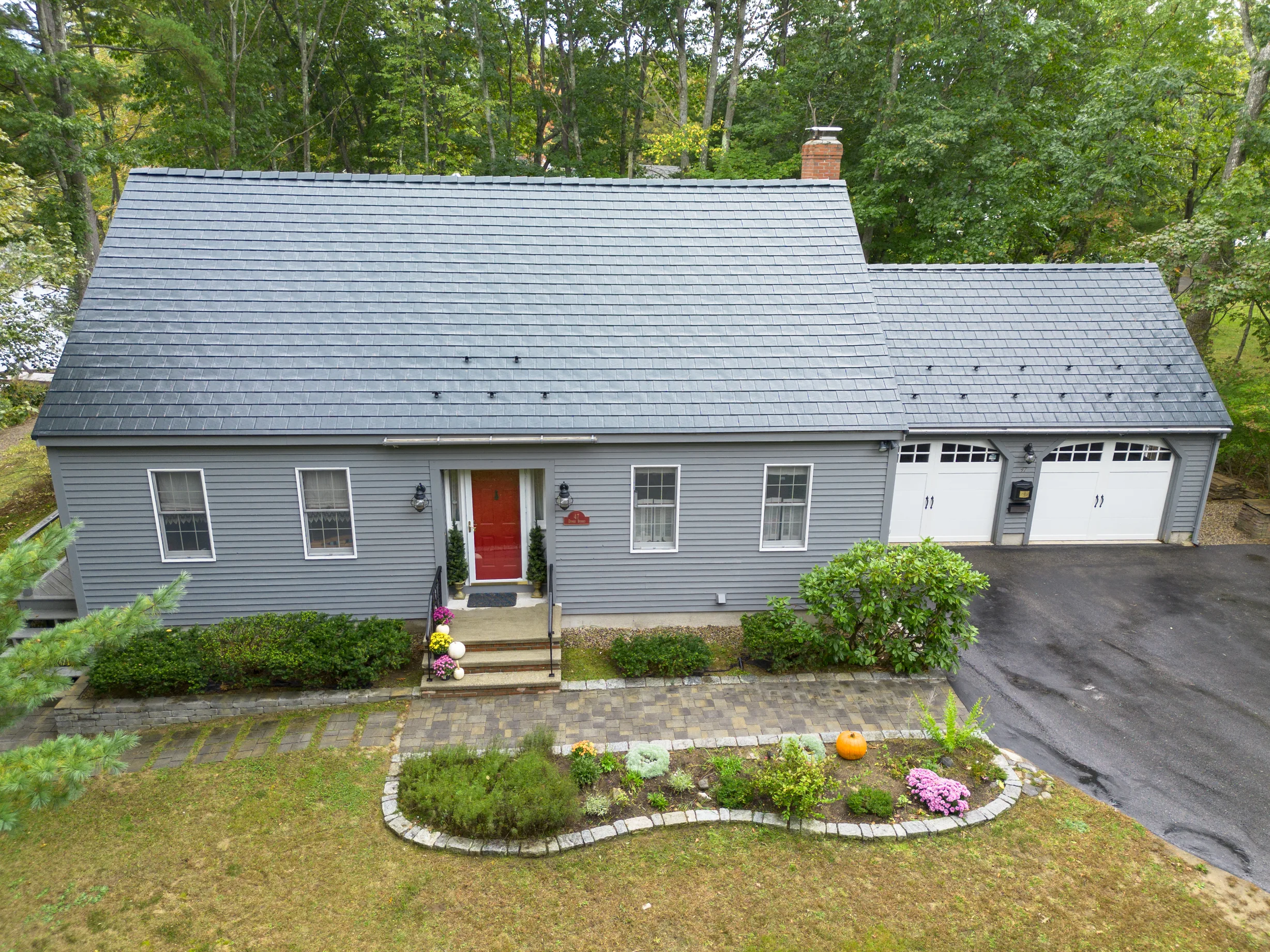 Black Interlock Slate aluminum roof on a grey two-storey home with a dormer among tall trees, Rochester, New Hampshire