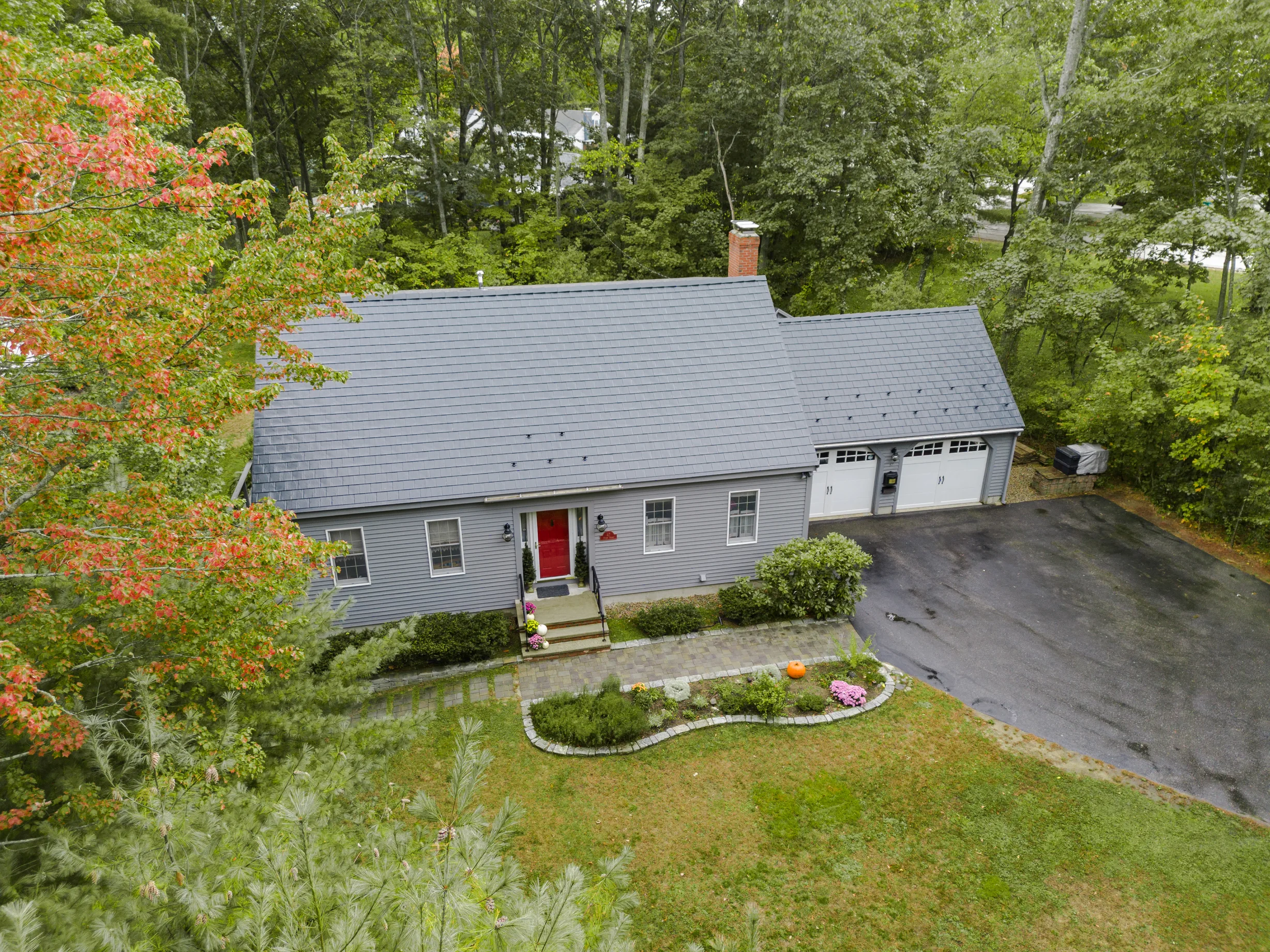 Black Interlock Slate aluminum roof on a grey single-family home with a metal roof among trees, Rochester, New Hampshire