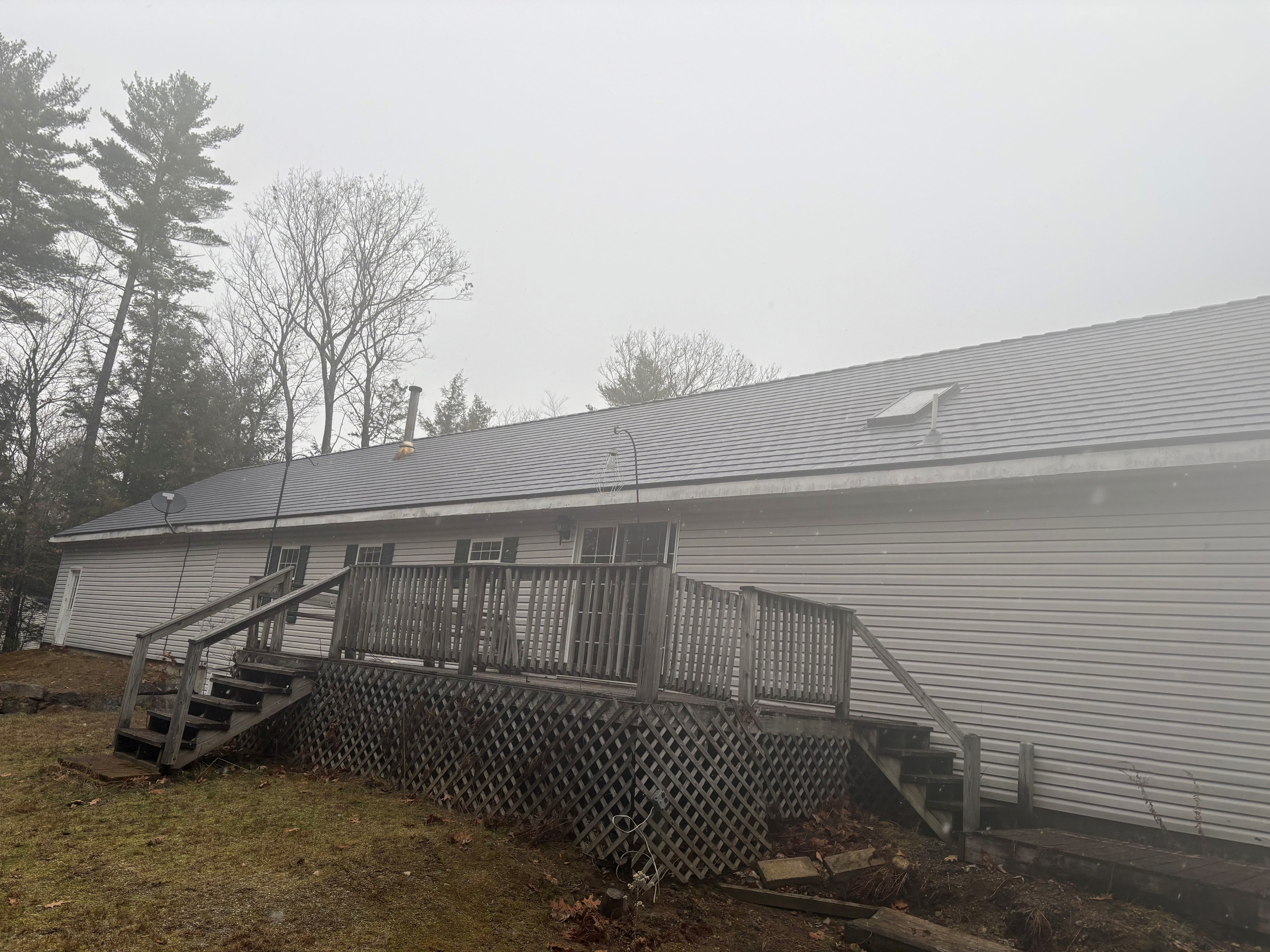 Rear elevation of a ranch-style home in New Hampton NH featuring Interlock deep charcoal aluminum slate metal roofing with a low-pitch gable and rear deck.