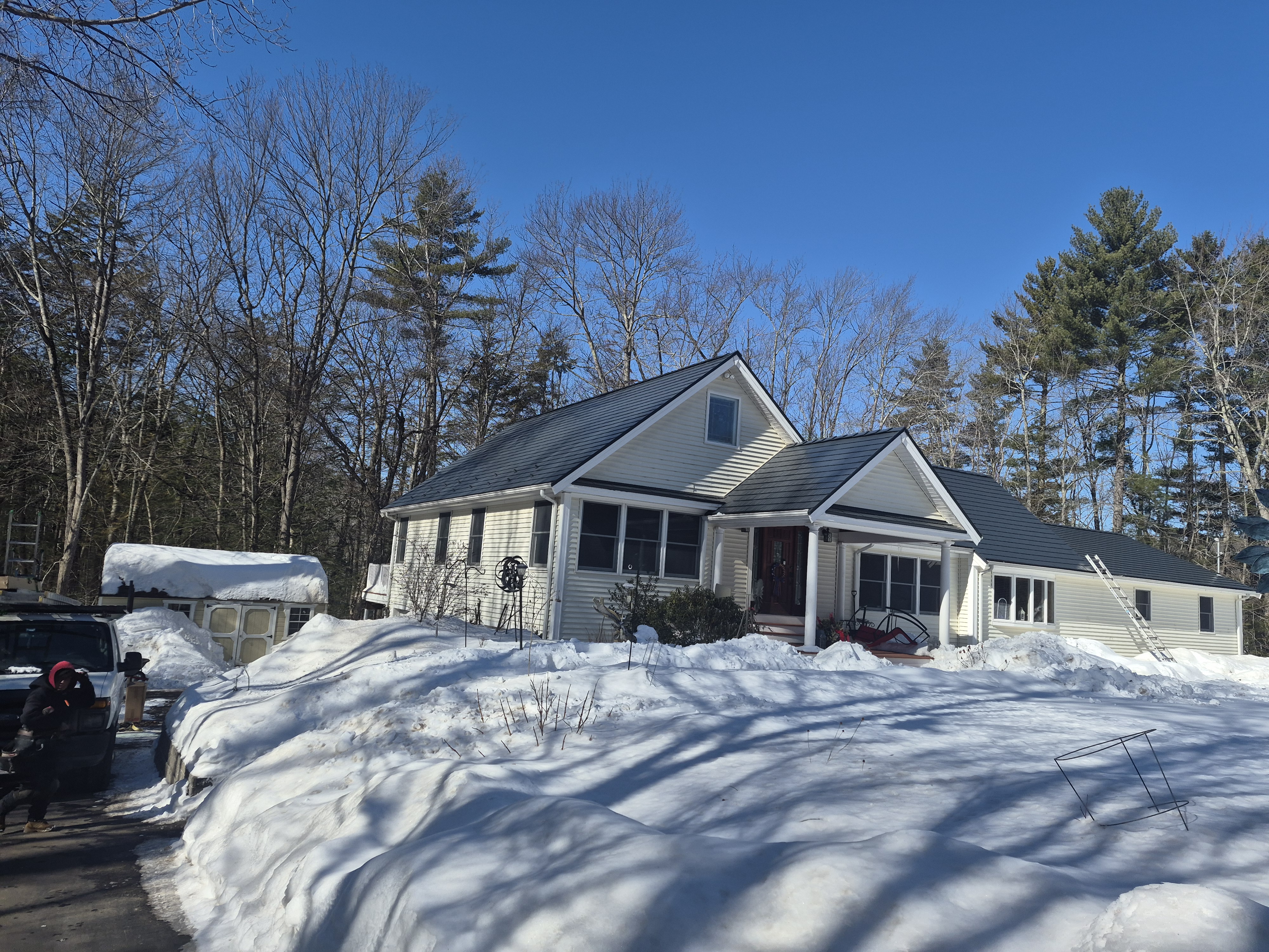 Cape Cod home in Epping NH with Interlock deep charcoal cedar shingle aluminum metal roof, front-left view amid heavy winter snow.