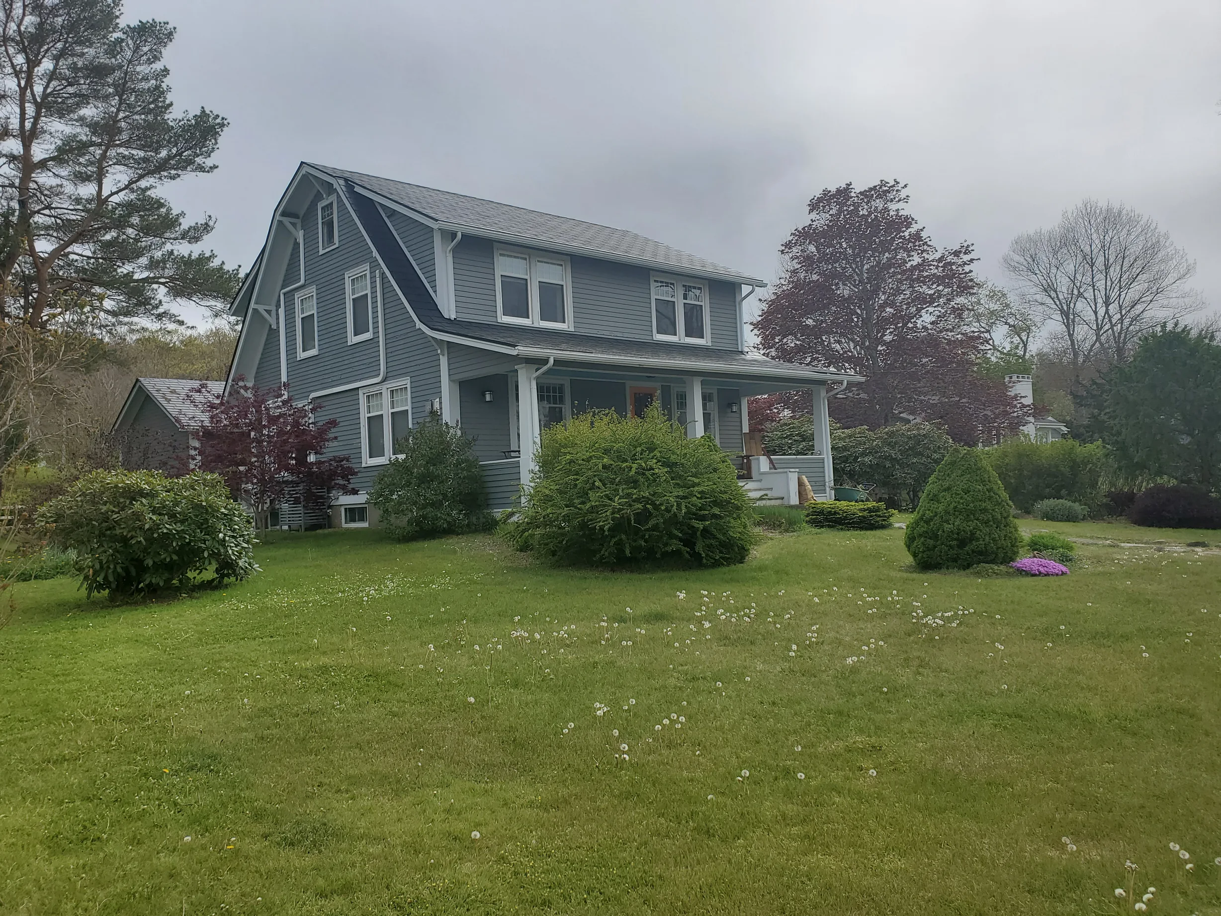 Black Interlock Slate aluminum roof on a green two-storey home with dormers in a lush green, Mahone Bay, Nova Scotia