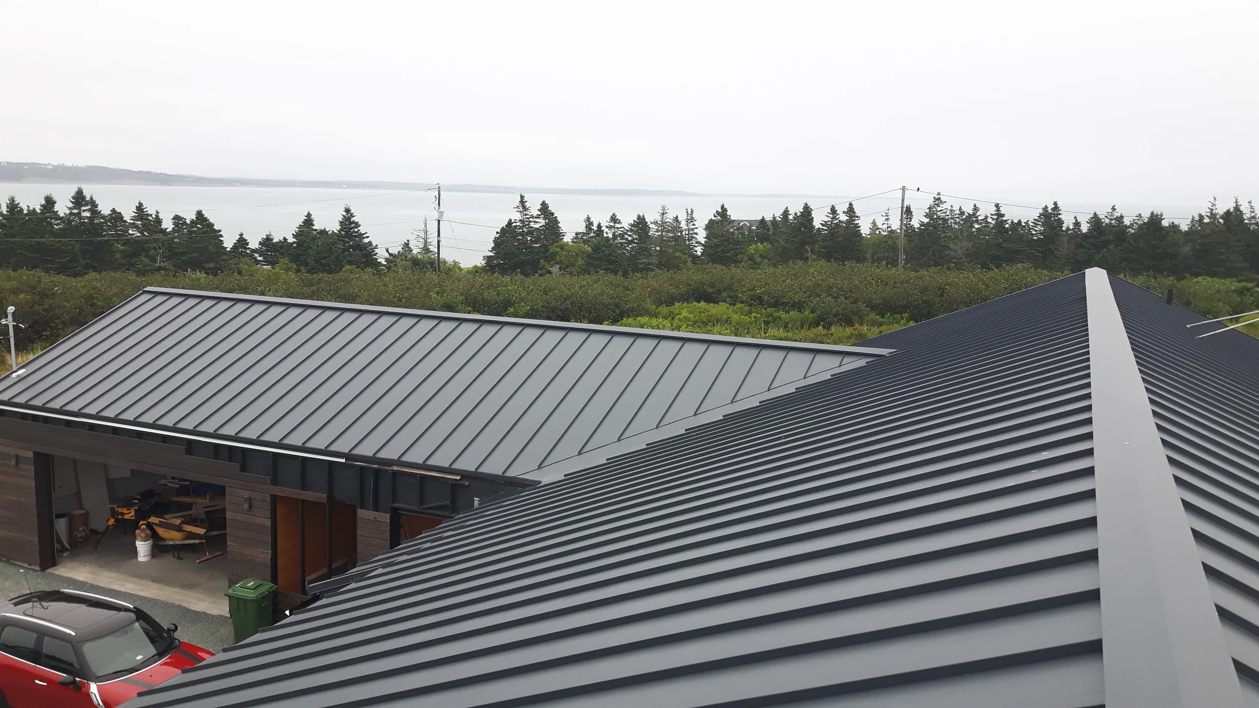 Deep Charcoal Interlock Standing Seam aluminum roof on a modern home with a metal roof among coastal trees, Cow Bay, Nova Scotia
