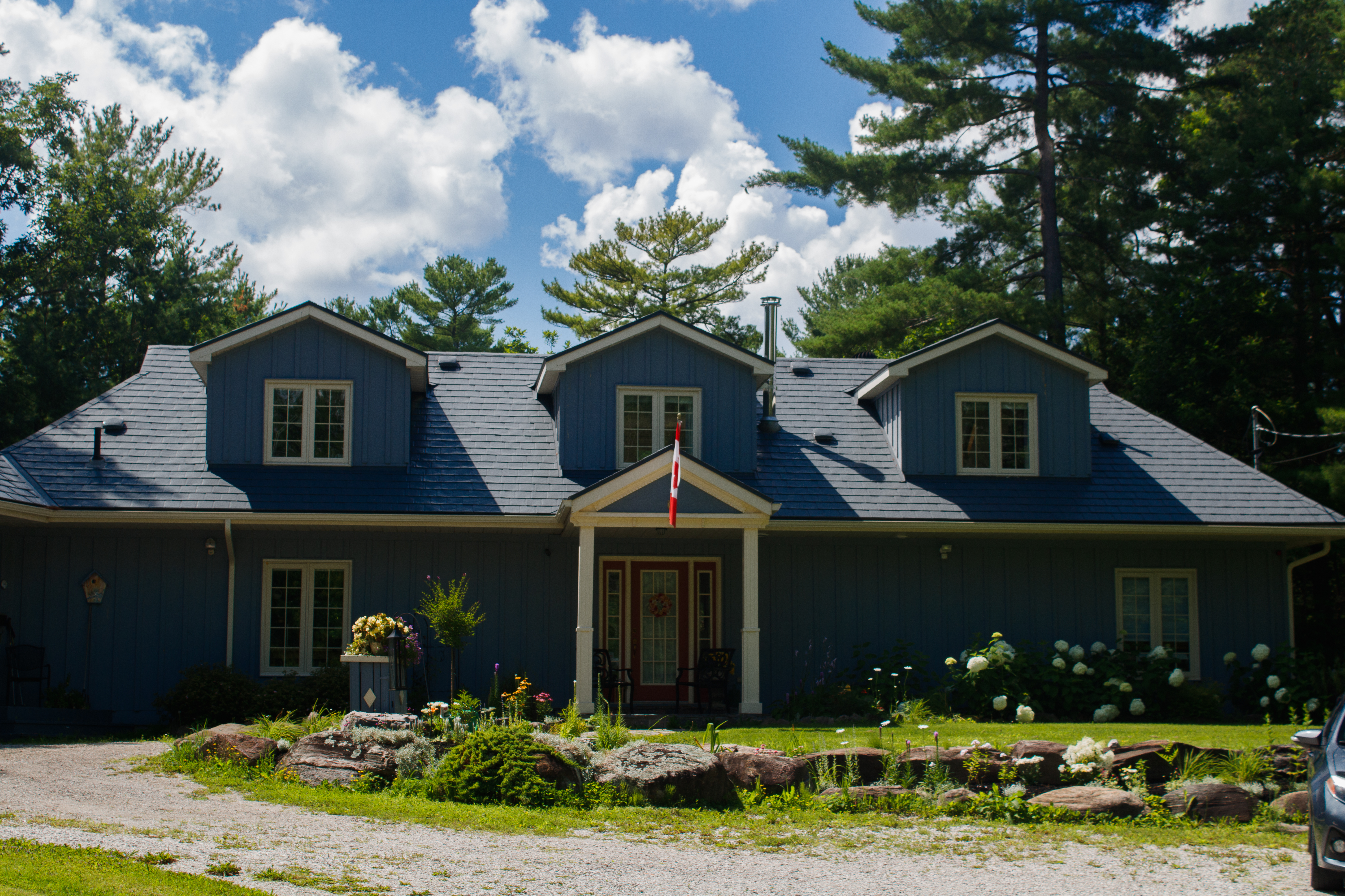 Front elevation of a blue board-and-batten home in Washago, ON with Interlock charcoal grey aluminum slate roofing, three dormers, and a covered entry porch.