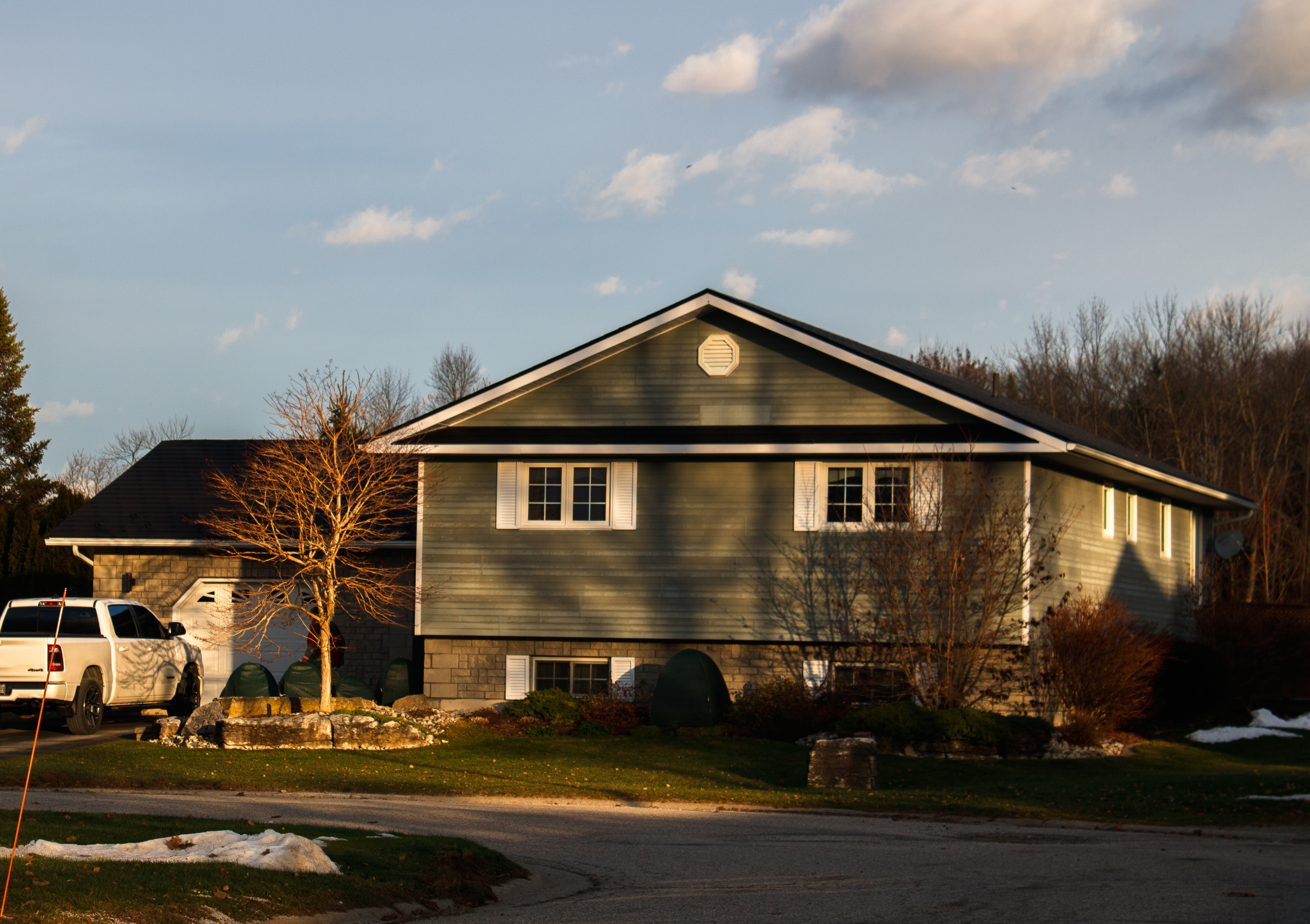 Bi-level single-family home in Wiarton ON with black Interlock aluminum slate metal roofing, simple gable profile, and octagonal roof louver at golden hour.