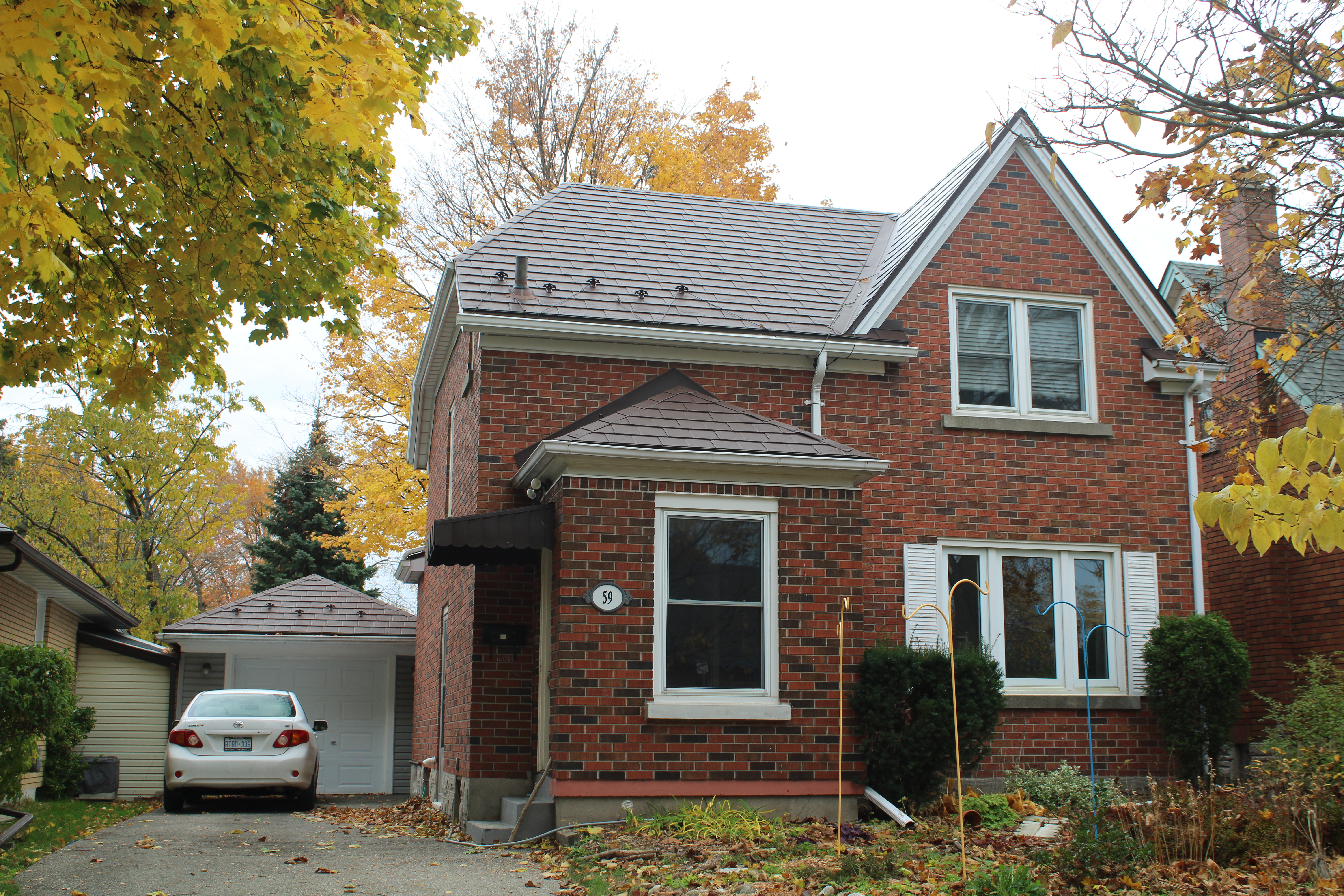 Two-storey red brick Tudor-style home in Kitchener ON with Interlock Colonial Brown aluminum slate metal roofing, hip and gable roof, surrounded by autumn foliage.