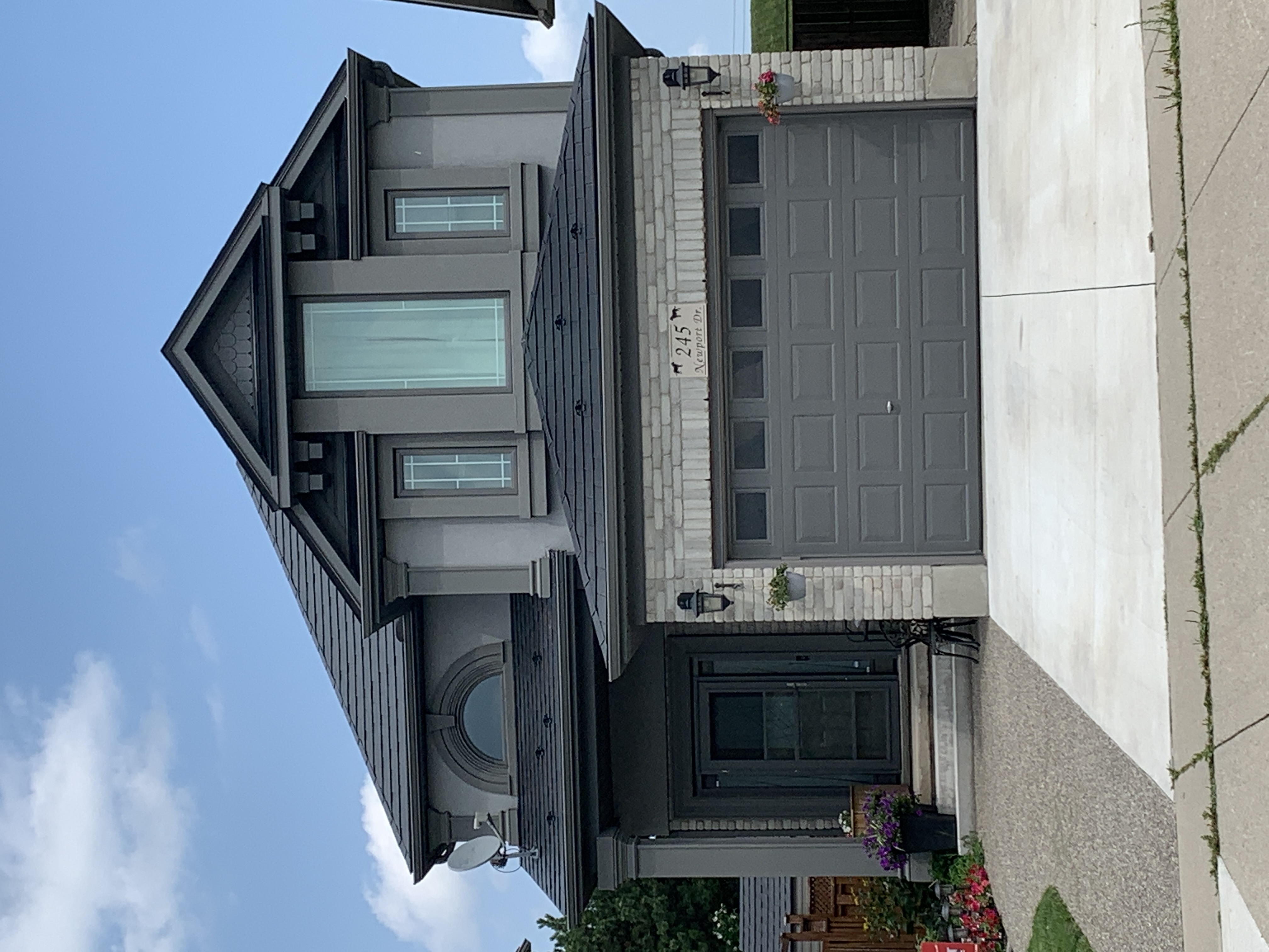 Two-storey Colonial home in Cambridge ON with black Interlock aluminum slate metal roof, complex multi-hip profile, dormer, and grey stucco and stone exterior.