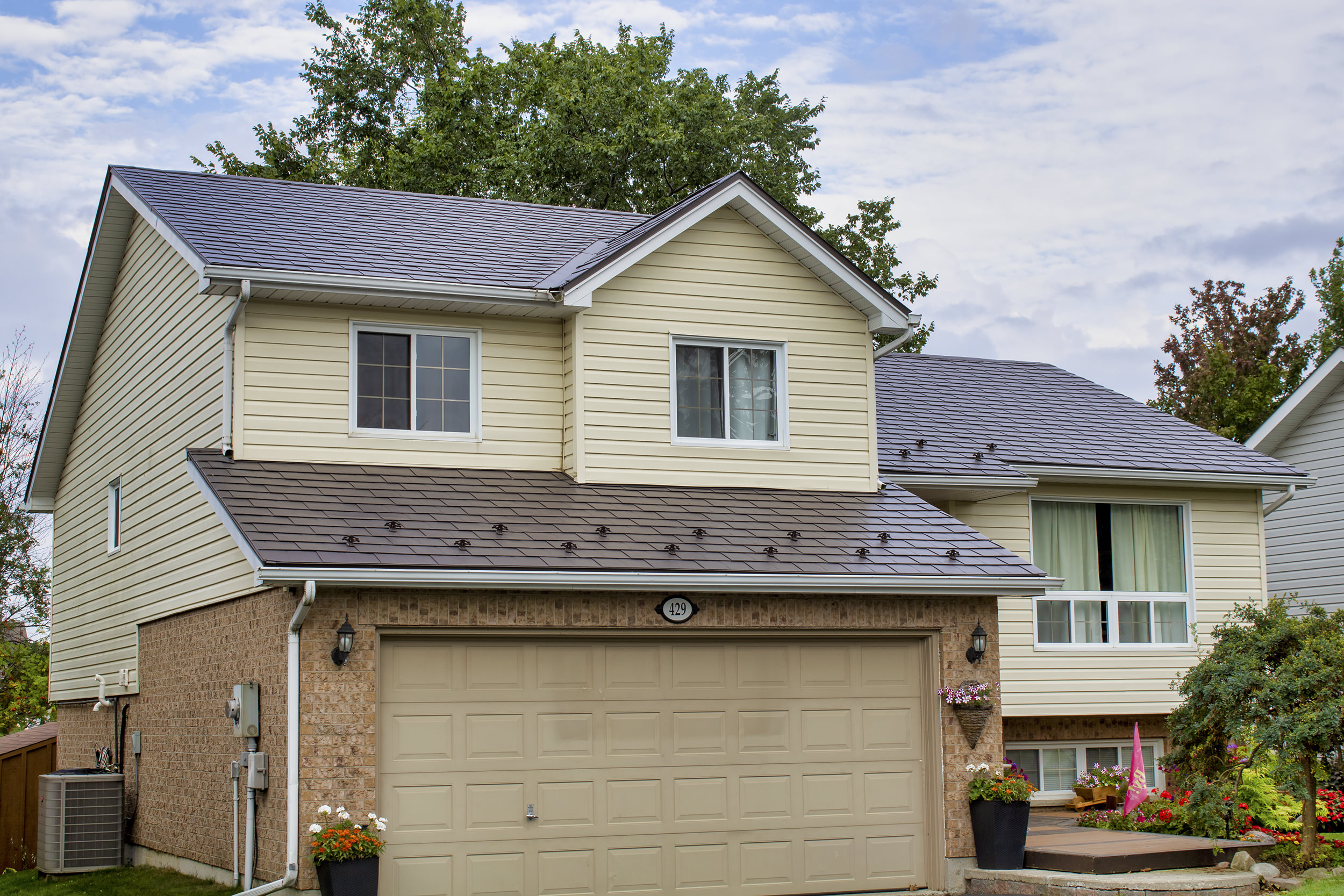 Two-storey colonial home in Shelburne ON featuring Interlock aluminum slate metal roofing in Tudor Brown across a multi-hip complex roof with cream vinyl siding.