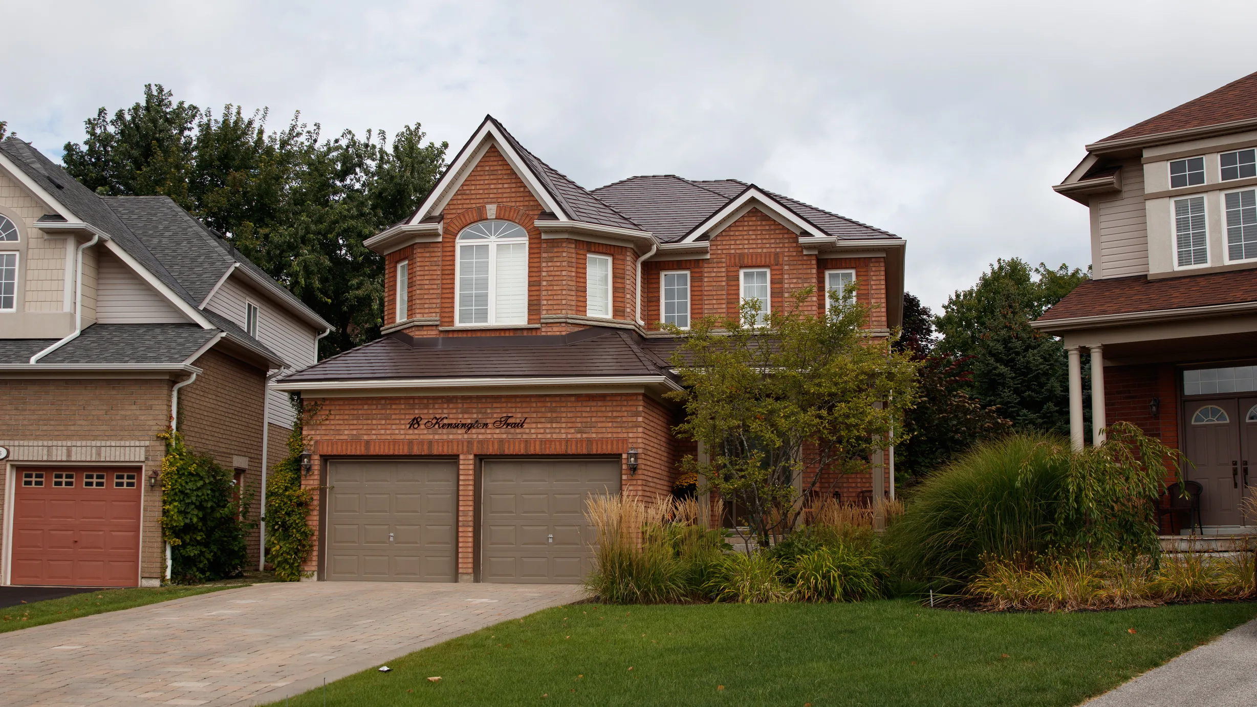 Tudor Brown Interlock Slate aluminum roof on a brown two-storey home with dormers among tall trees, Barrie, Ontario