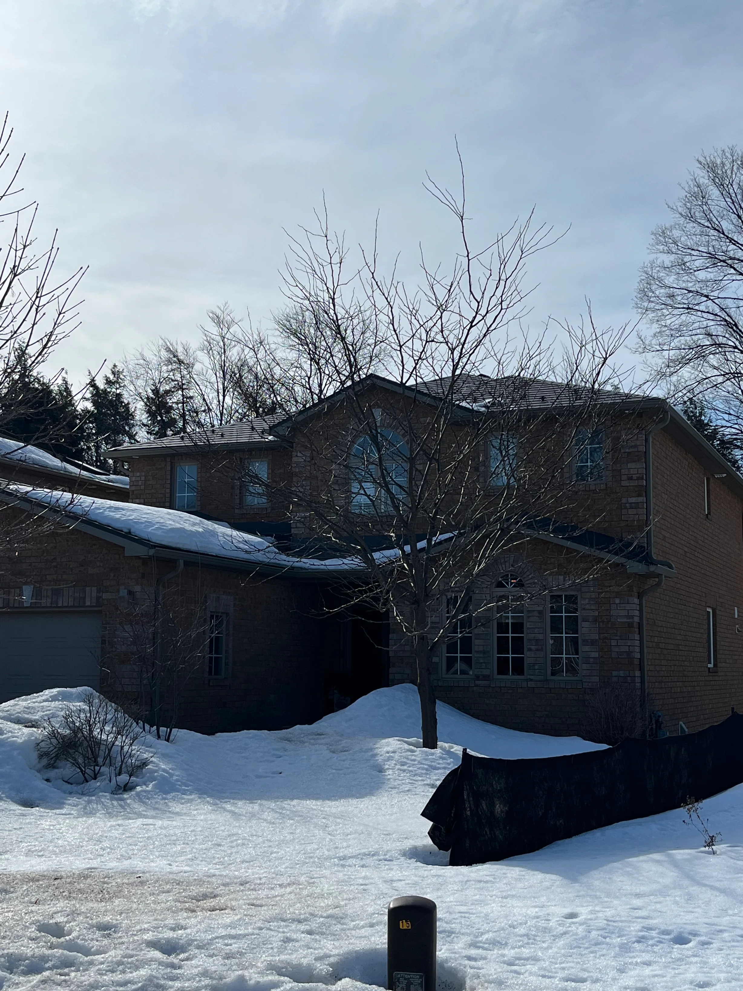 Musket Grey Interlock Slate aluminum roof being installed on a two-storey home in a forested area with snow on the ground, Barrie, Ontario