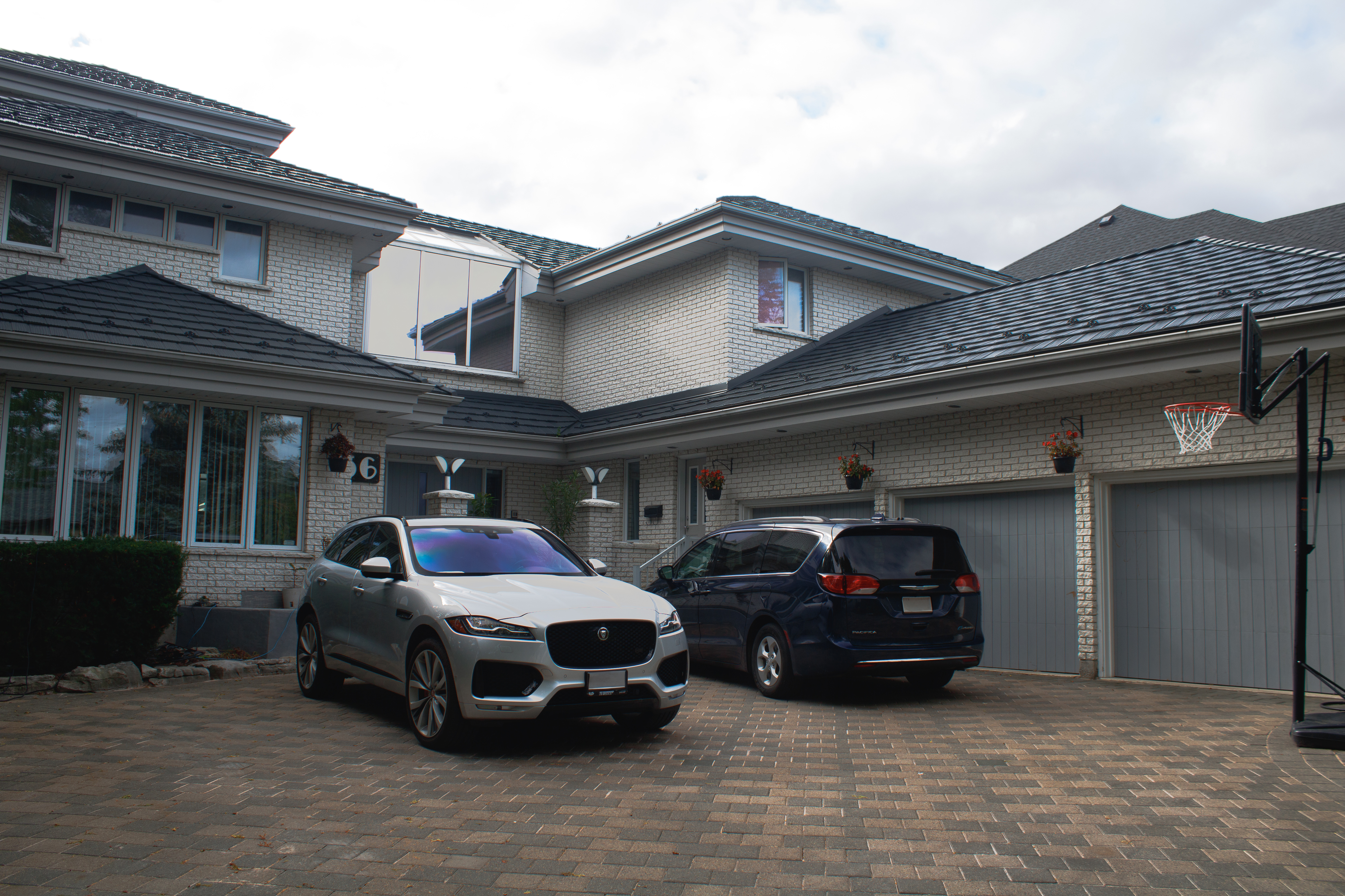 Two-storey white brick home in Whitby ON with Interlock charcoal grey aluminum shake metal roofing across a complex multi-hip roof, viewed from the front driveway.