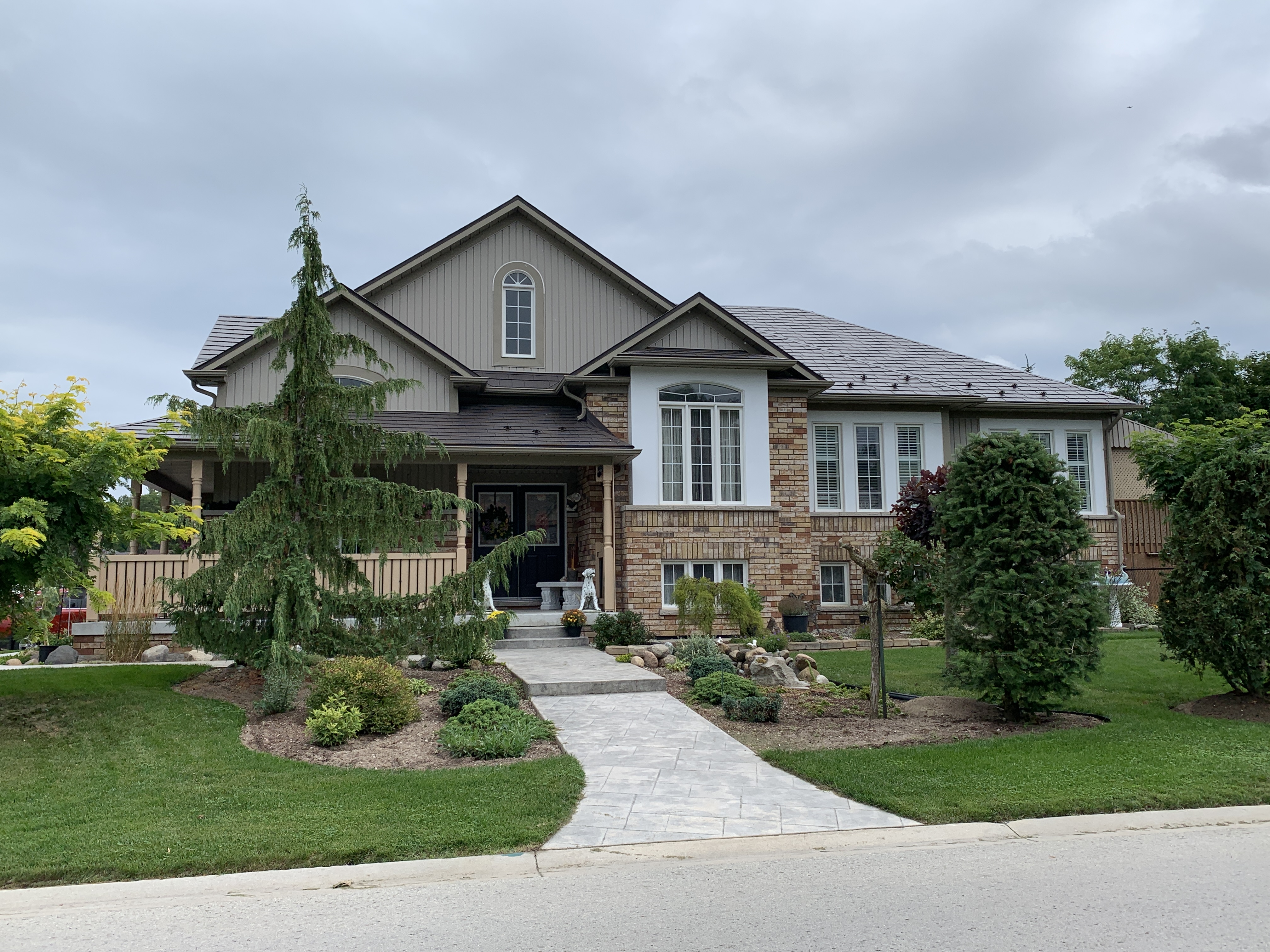 Craftsman-style brick home in Wasaga Beach with Interlock Tudor Brown aluminum slate metal roofing, multi-hip complex roofline, and landscaped front yard.