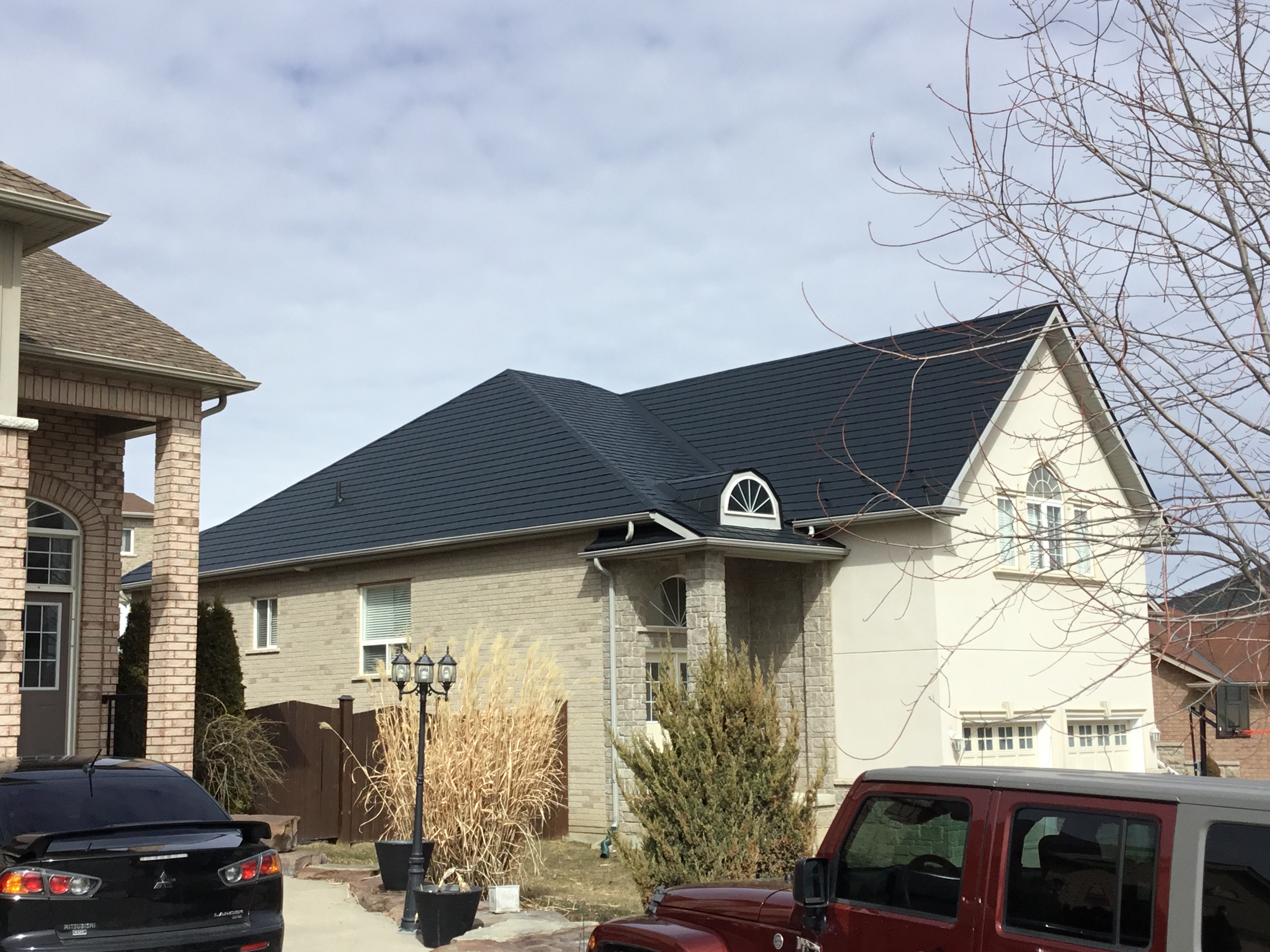 Black Interlock aluminum slate metal roof on a 1.5-storey suburban home in Bradford, featuring a complex hip profile and arched dormer window.