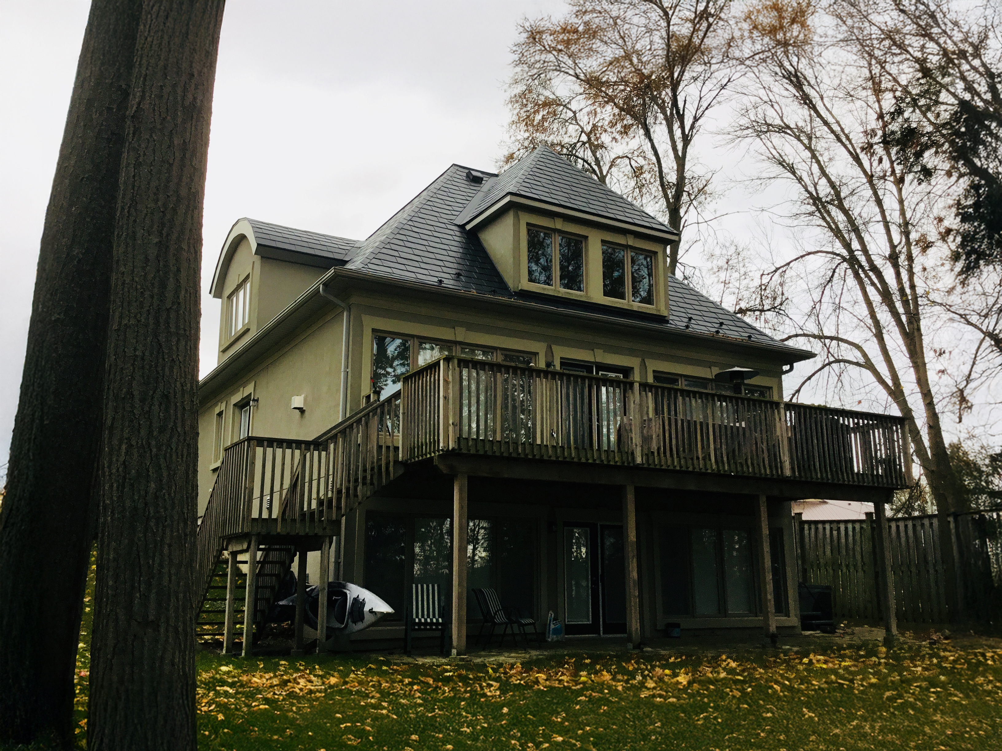 Rear elevation of a 3-storey Victorian home in Orillia ON featuring black Interlock aluminum slate roofing with a central turret, dormer, and large elevated wood deck.