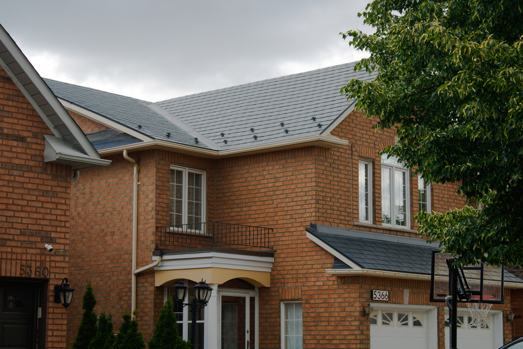 Two-storey suburban brick townhome with deep charcoal Interlock aluminum slate metal roof featuring snow guards on a complex multi-hip roofline.