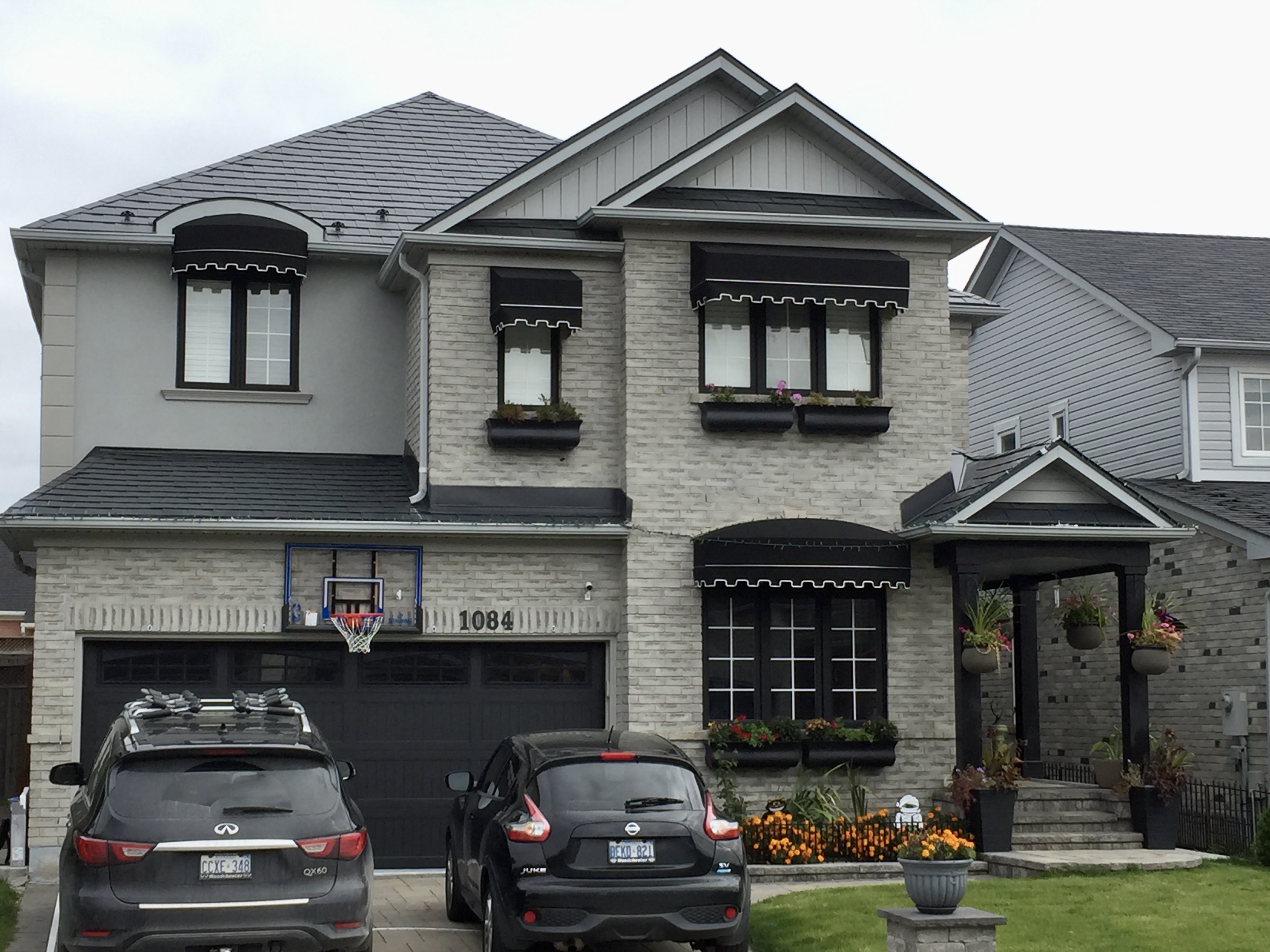 Two-storey craftsman home in Milton ON with black Interlock aluminum slate metal roofing, light grey brick facade, black awnings, and window boxes.