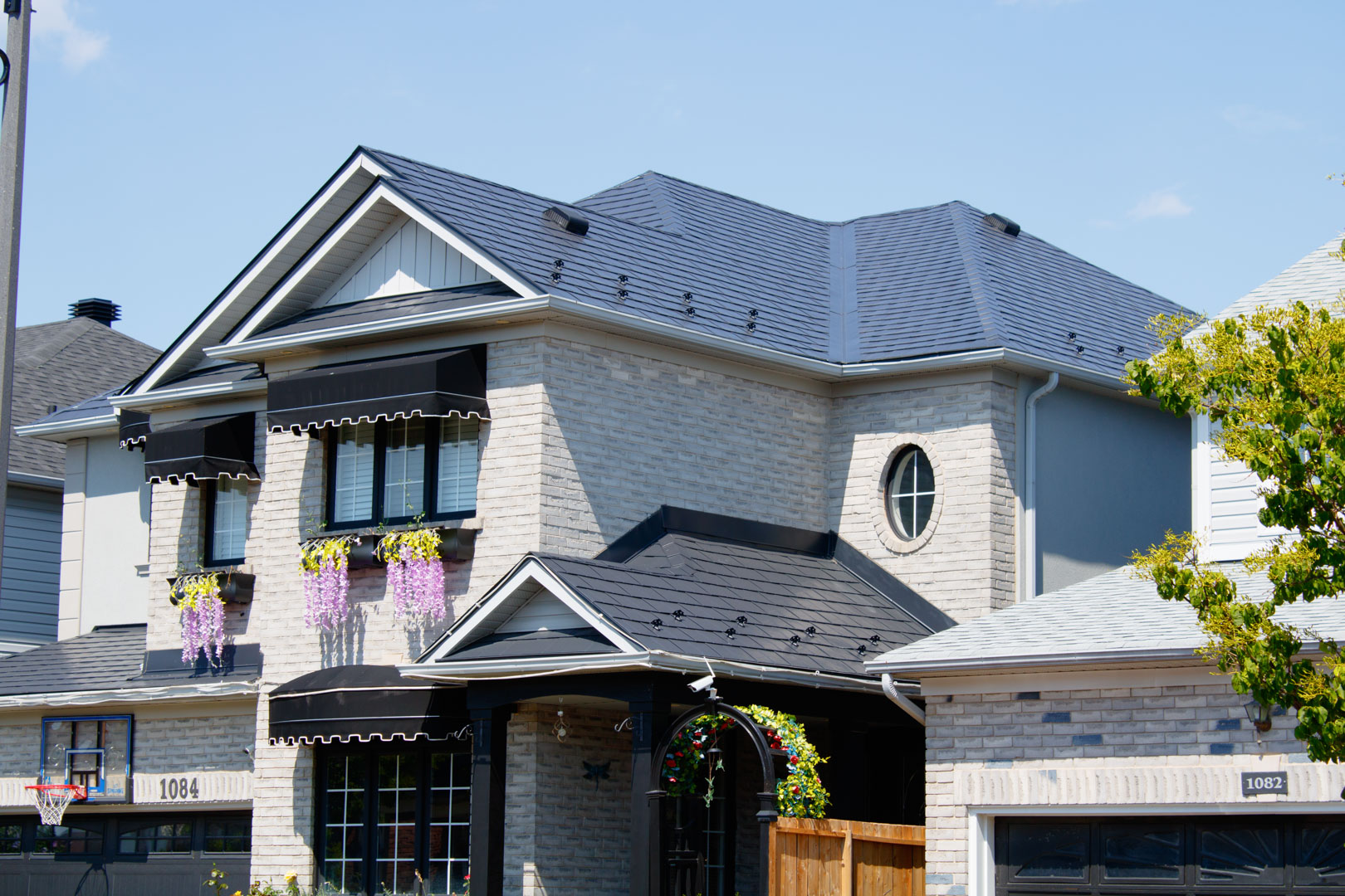 Two-storey brick home in Milton ON with a complex multi-hip black Interlock aluminum slate metal roof featuring dormers and decorative awnings.