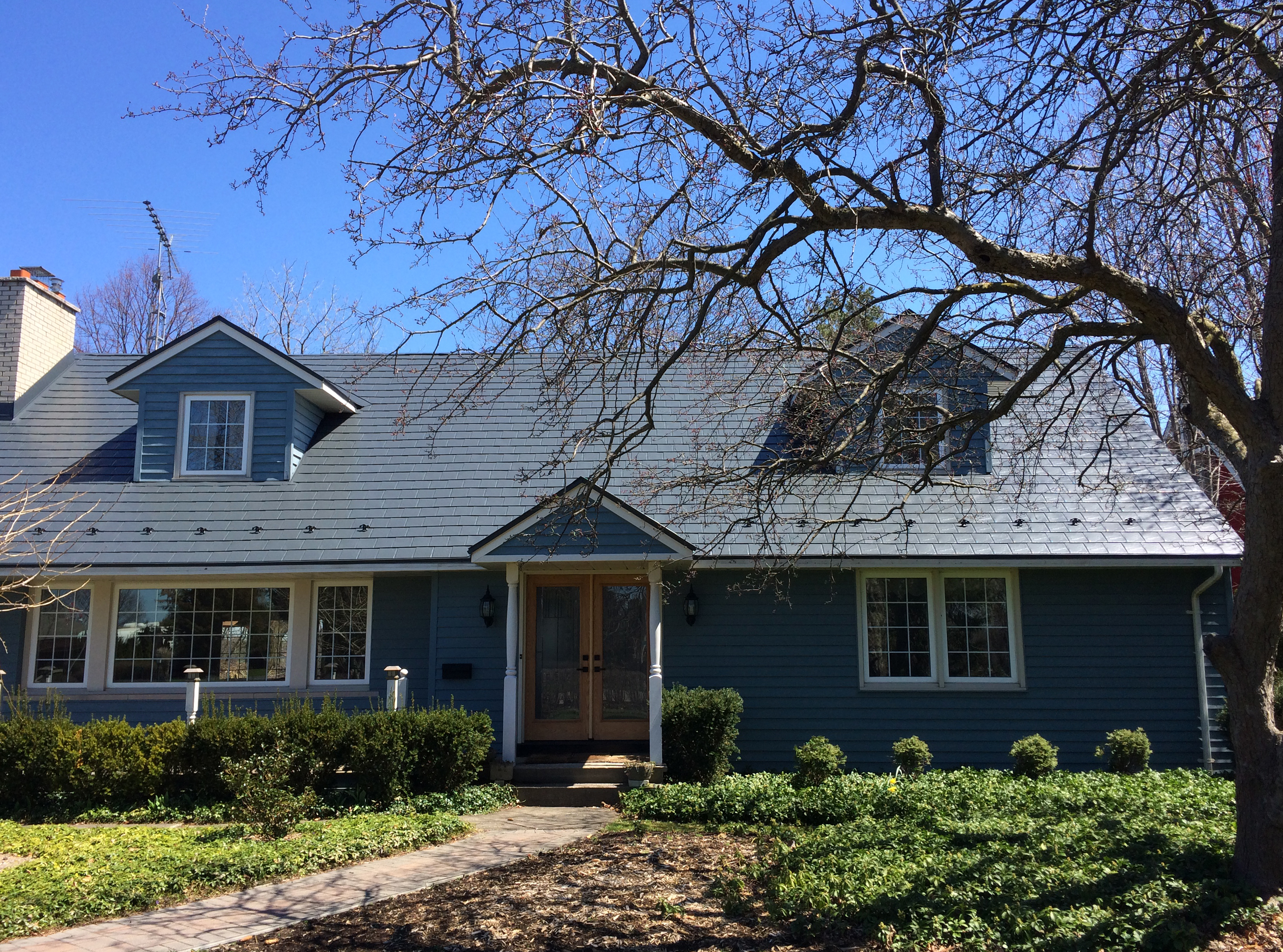 Cape Cod home with Interlock deep charcoal aluminum slate metal roof, twin dormers, snow guards, and blue siding in Niagara on the Lake.