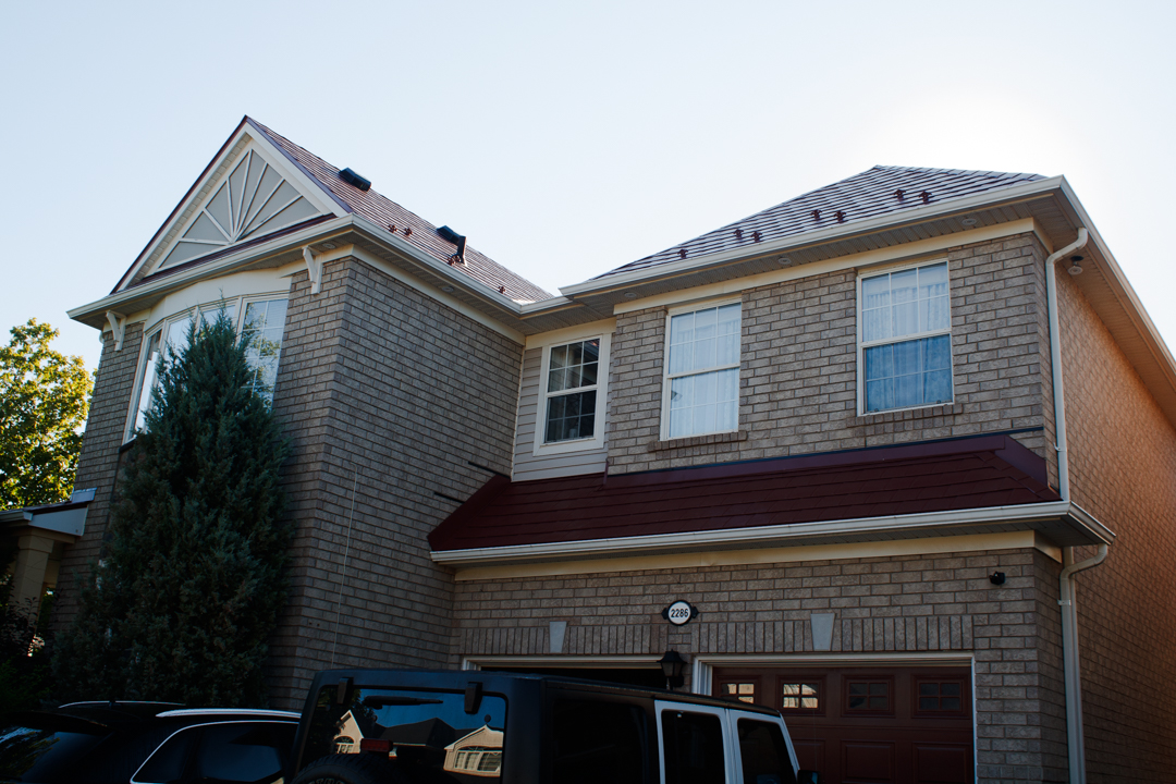 Two-storey colonial brick home in Oakville with Interlock tile-red aluminum slate metal roofing across complex multi-hip and gable roof planes.