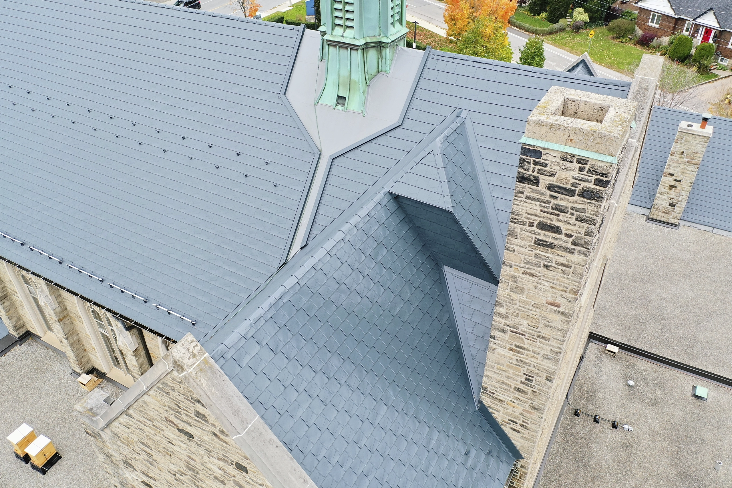 Aerial view of a deep charcoal Interlock aluminum slate roof on a historic stone church in Toronto, featuring complex valleys, a patinated copper spire, and stone chimneys.