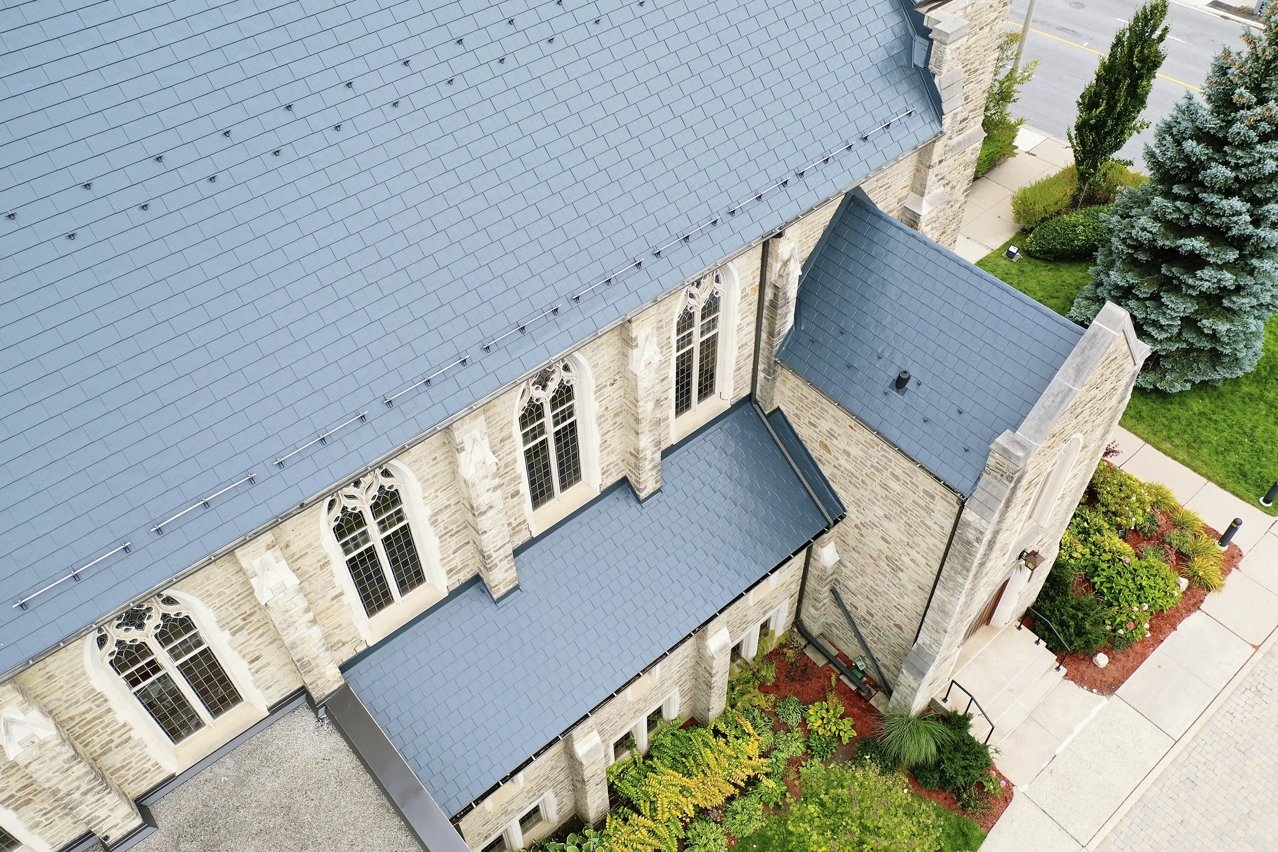 Aerial view of a Gothic stone church in Toronto with a deep charcoal Interlock aluminum slate roof featuring snow rails, complex valleys, and Gothic arched windows.