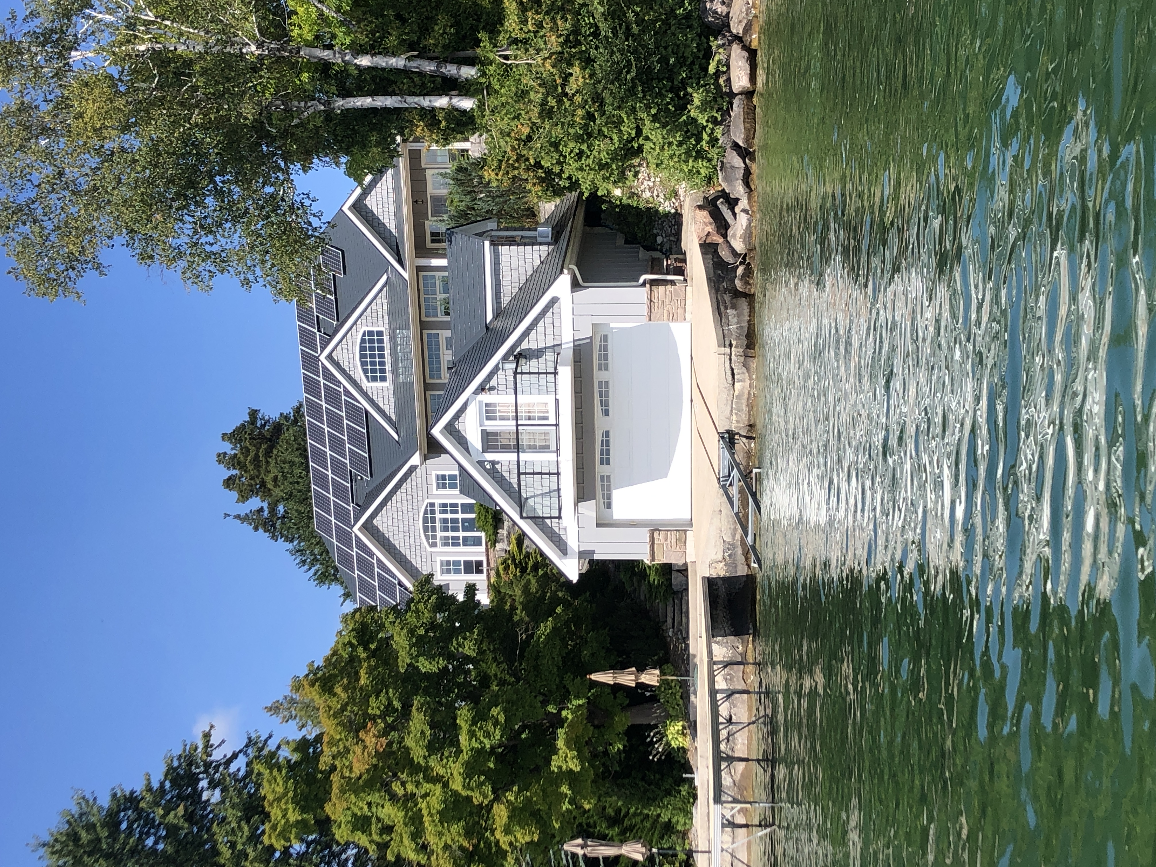 Large Craftsman lakefront home in Shanty Bay, ON with deep charcoal Interlock aluminum slate roofing, multiple dormers, and solar panels viewed from the water.