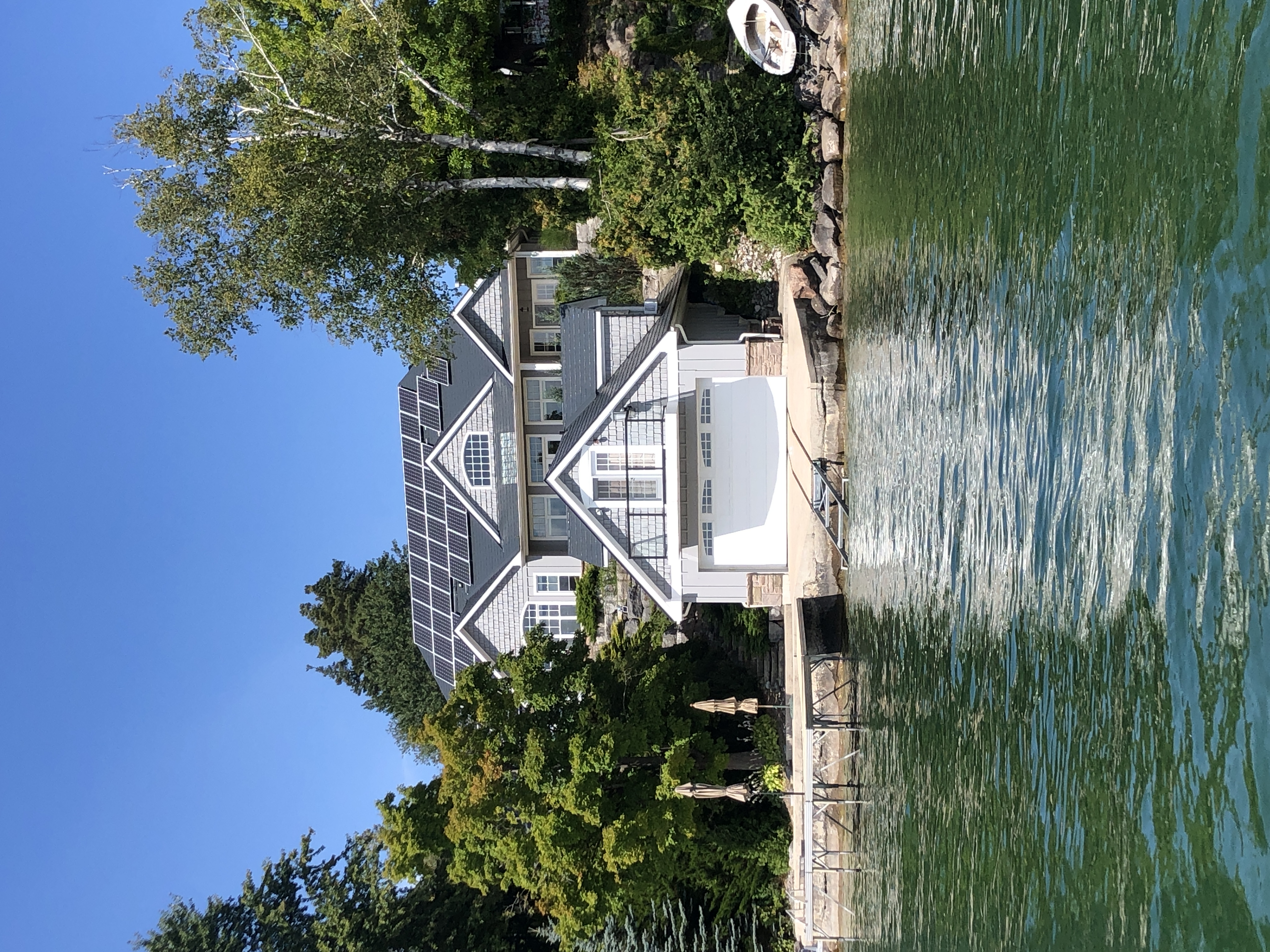 Large Craftsman lakefront home in Shanty Bay, ON with deep charcoal Interlock aluminum slate roof, solar panels, and a boathouse at water's edge.