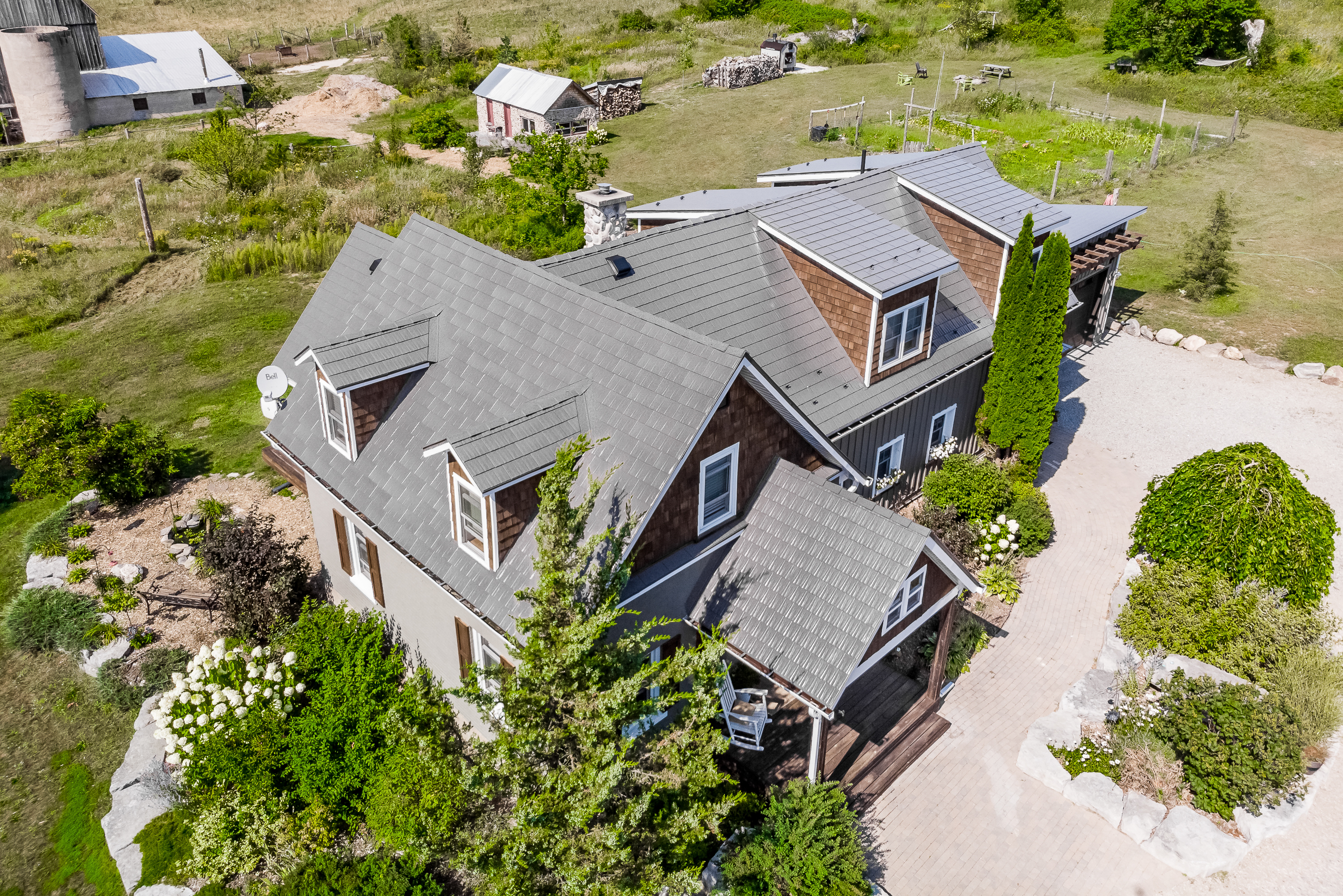 Aerial view of a complex multi-hip Interlock aluminum cedar shingle roof in Weathered finish on a rural Craftsman-style two-storey home in Midland, ON.