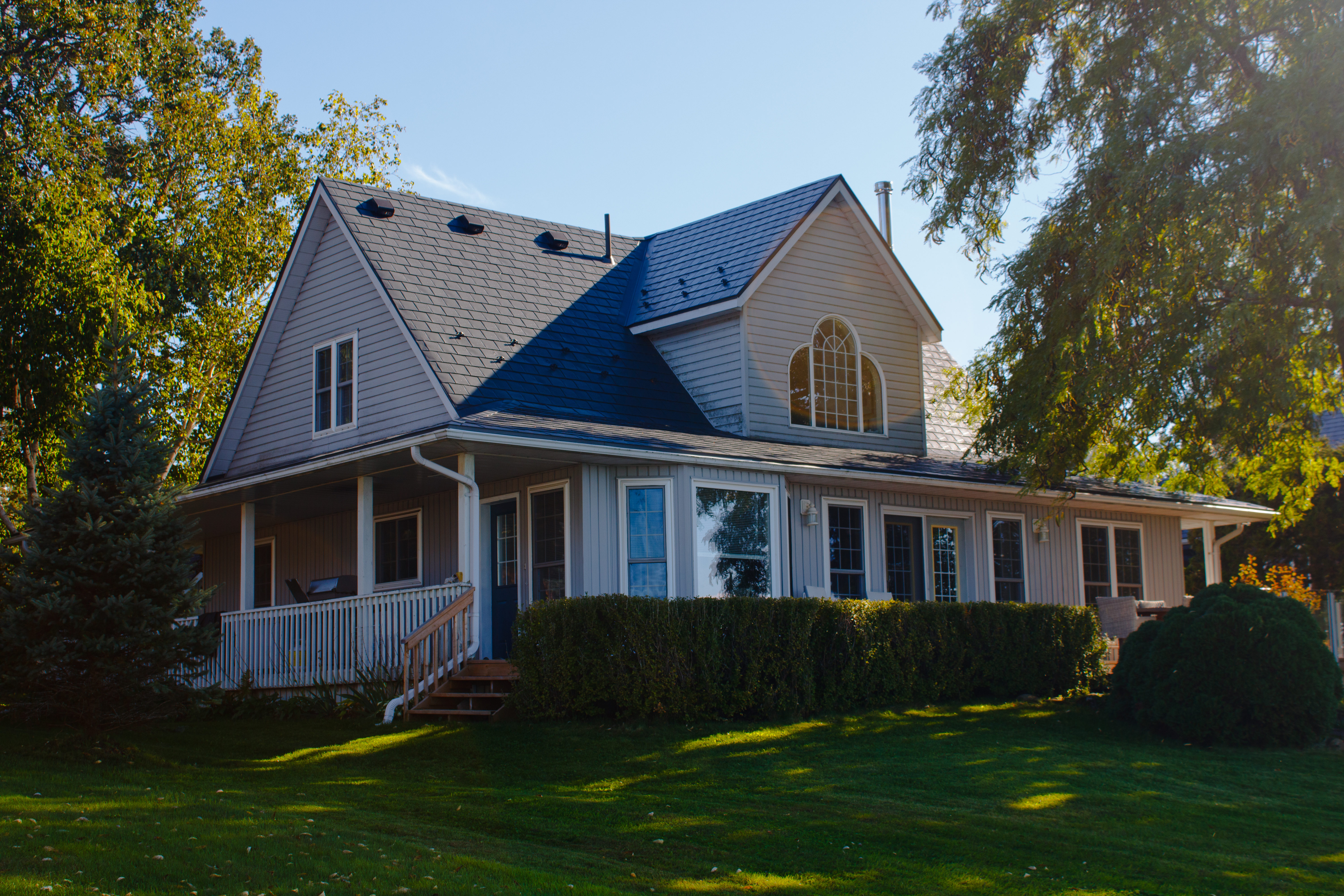 1.5-storey Craftsman home in Cannifton, ON with deep charcoal Interlock aluminum slate metal roof featuring dormers, wraparound porch, and arched upper window.