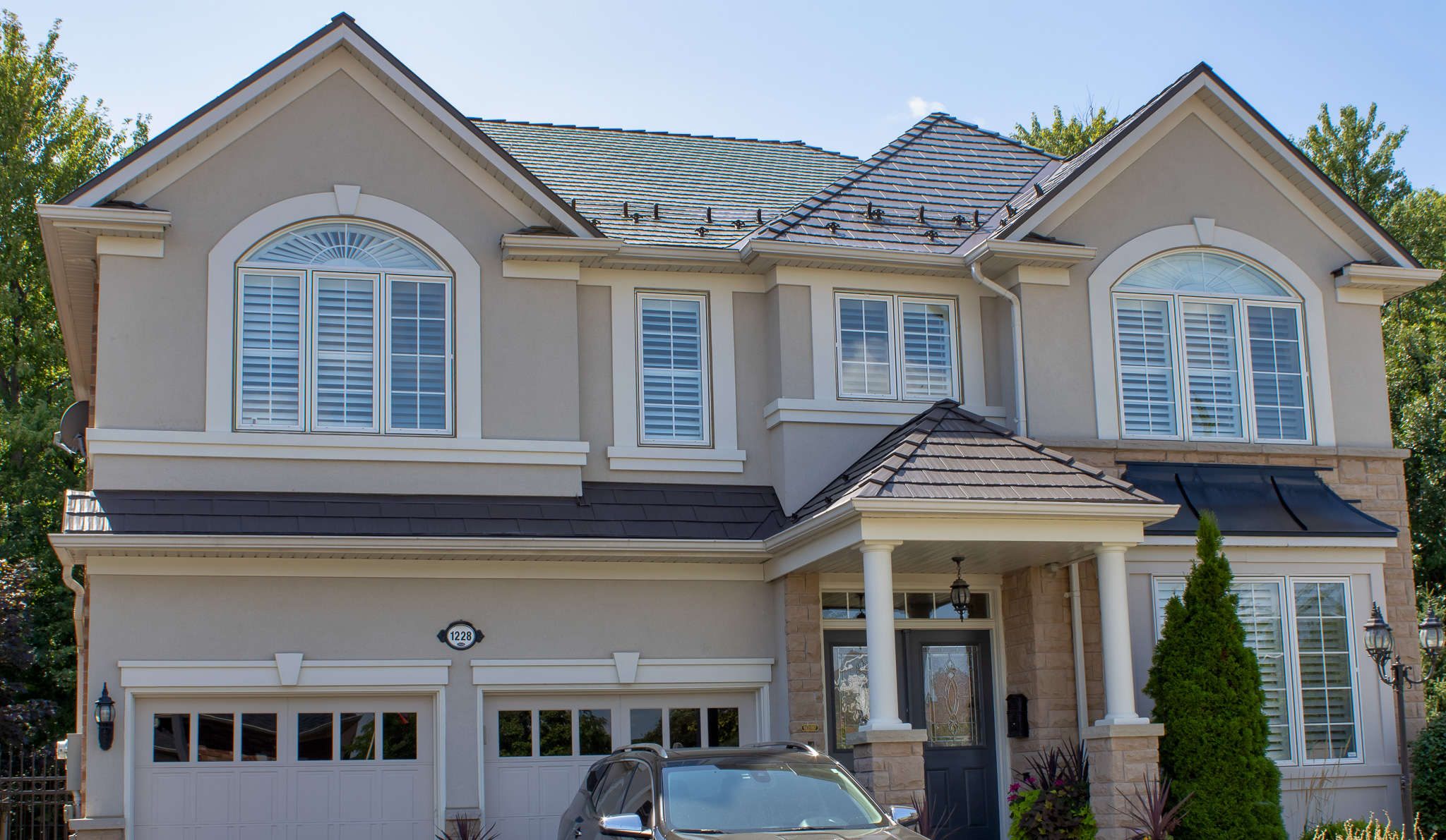 Two-storey suburban home in Milton ON with Interlock Tudor Brown cedar shingle metal roofing across a complex multi-hip roof with portico and attached garage.