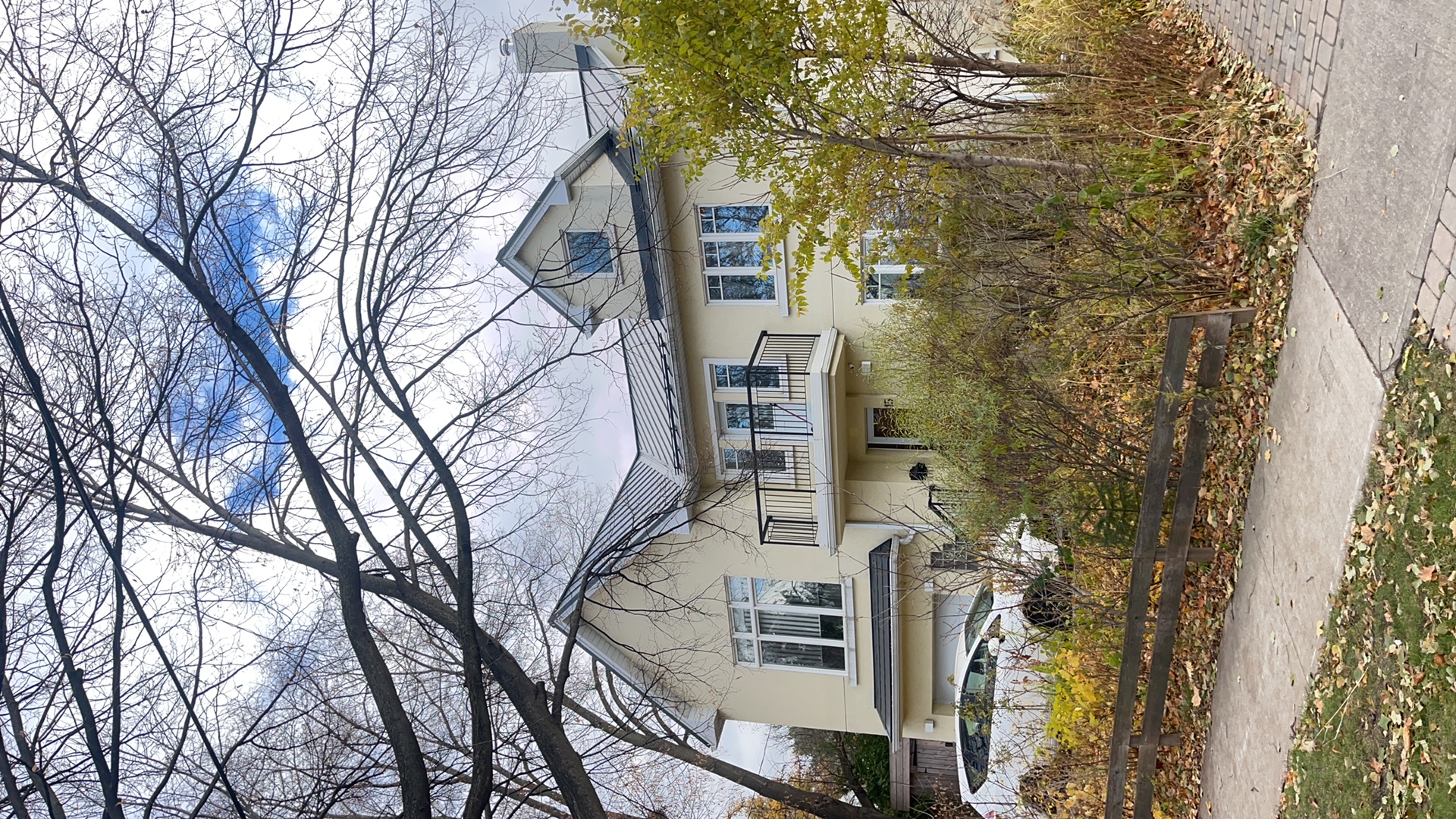 Two-storey Etobicoke home with deep charcoal standing seam metal roof featuring dormers and complex multi-plane roofline, photographed from street in autumn.