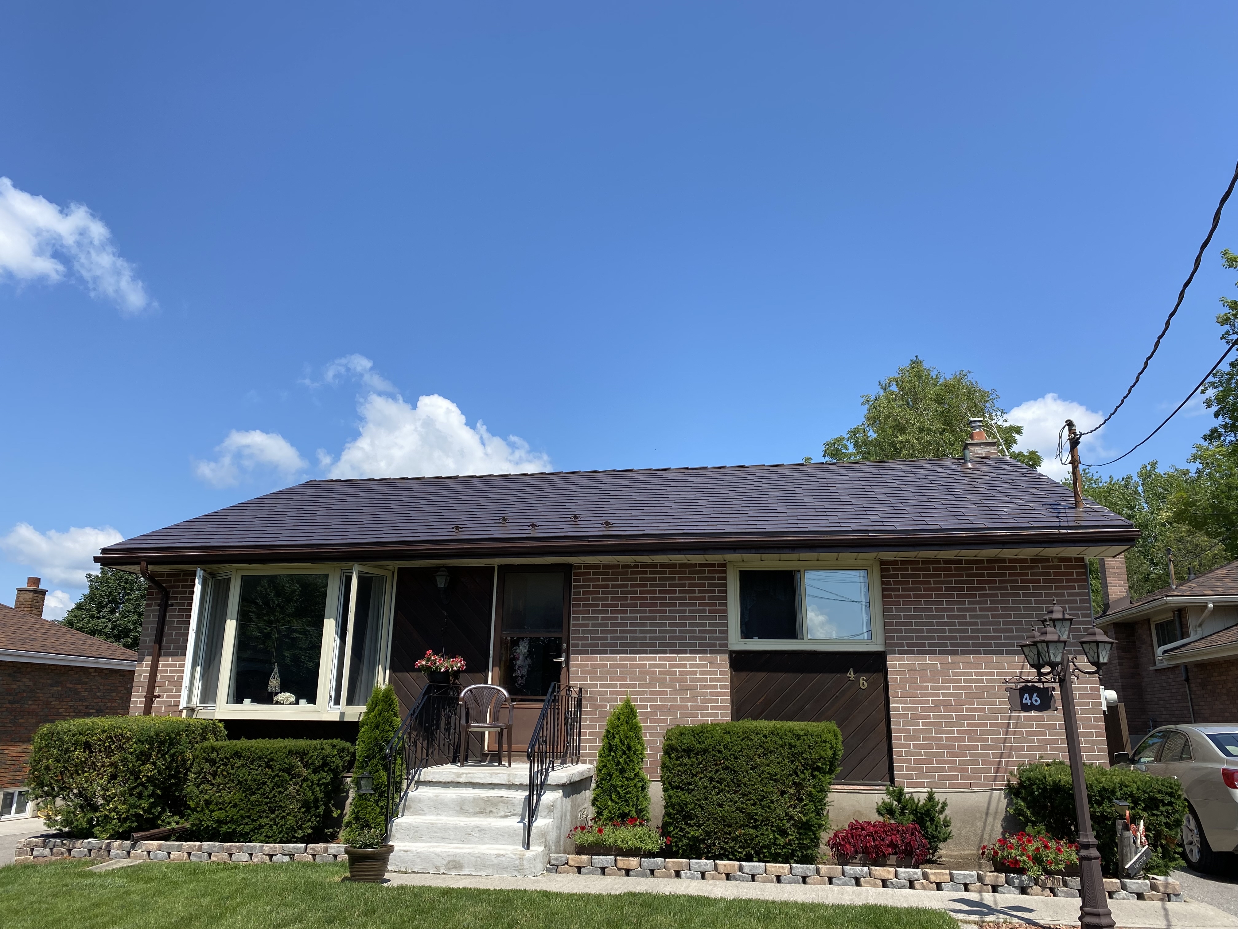 Single-storey ranch-style brick home in Belleville, ON, with a low-pitch Interlock aluminum slate roof in Colonial Brown under a bright blue sky.
