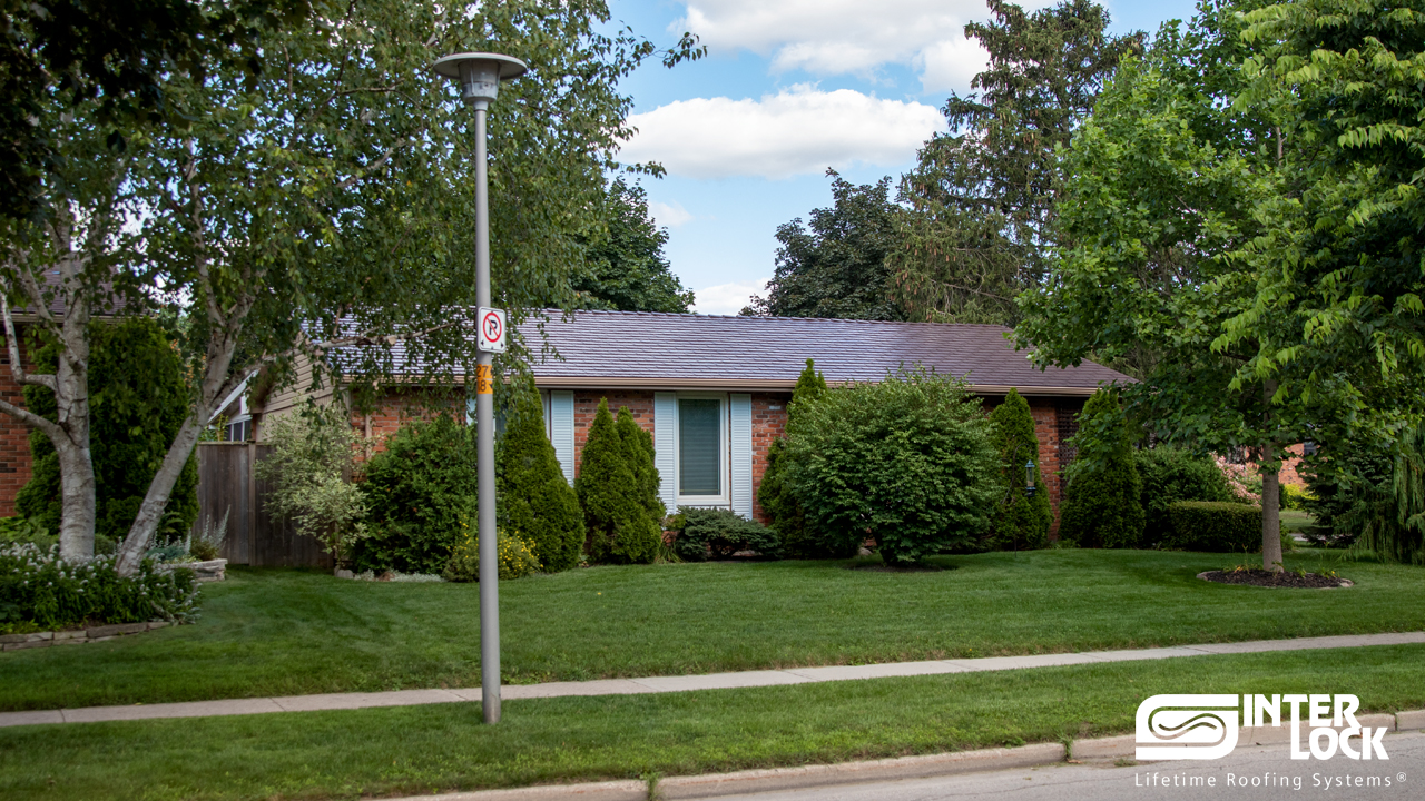 Single-storey ranch-style brick home with Interlock Colonial Brown cedar shingle aluminum roof, low-slope hip profile, lush landscaping.