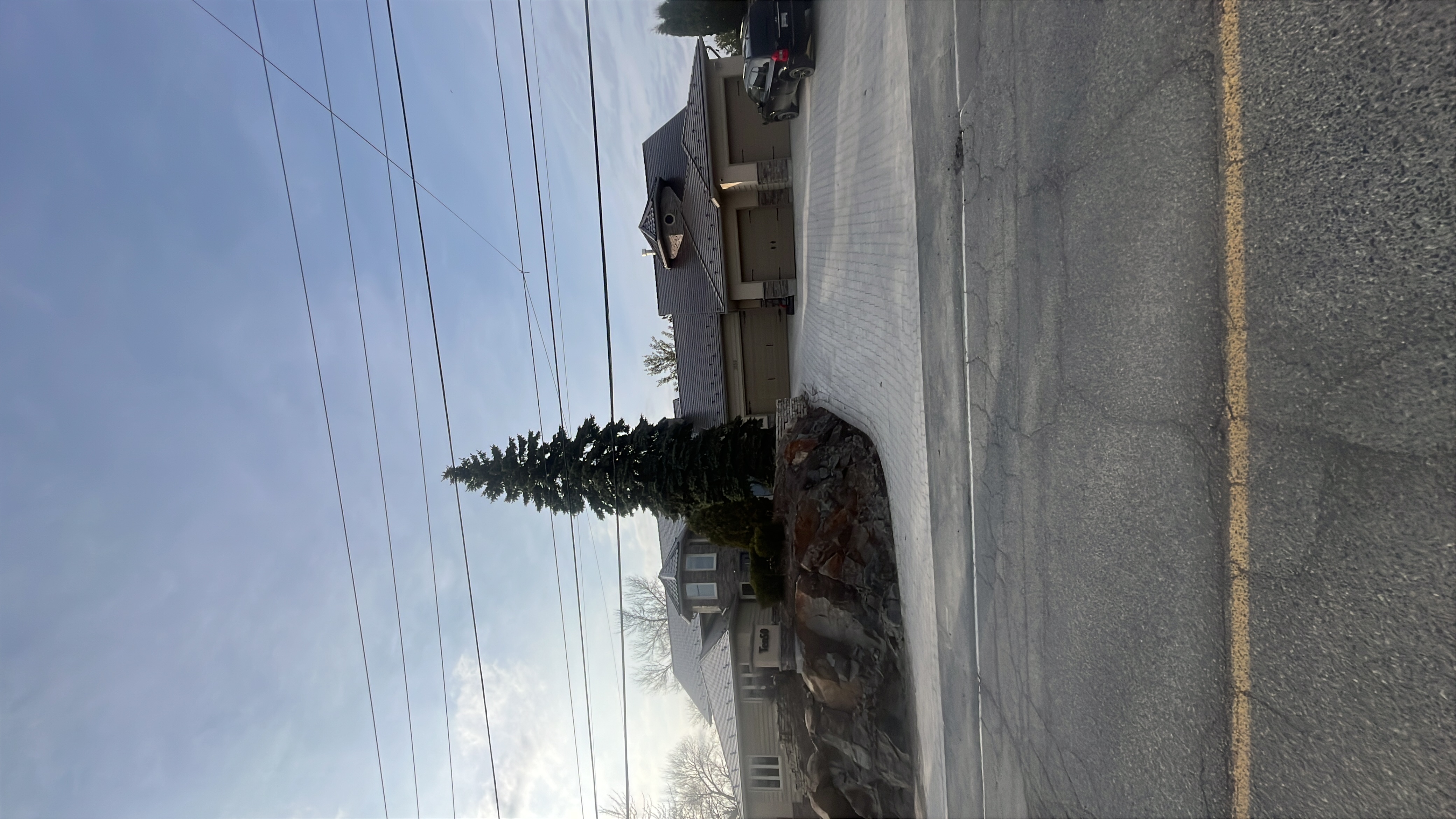 Street-view of a large suburban home in Sudbury with Interlock Colonial Brown aluminum slate roofing across a complex multi-hip profile with turret feature.