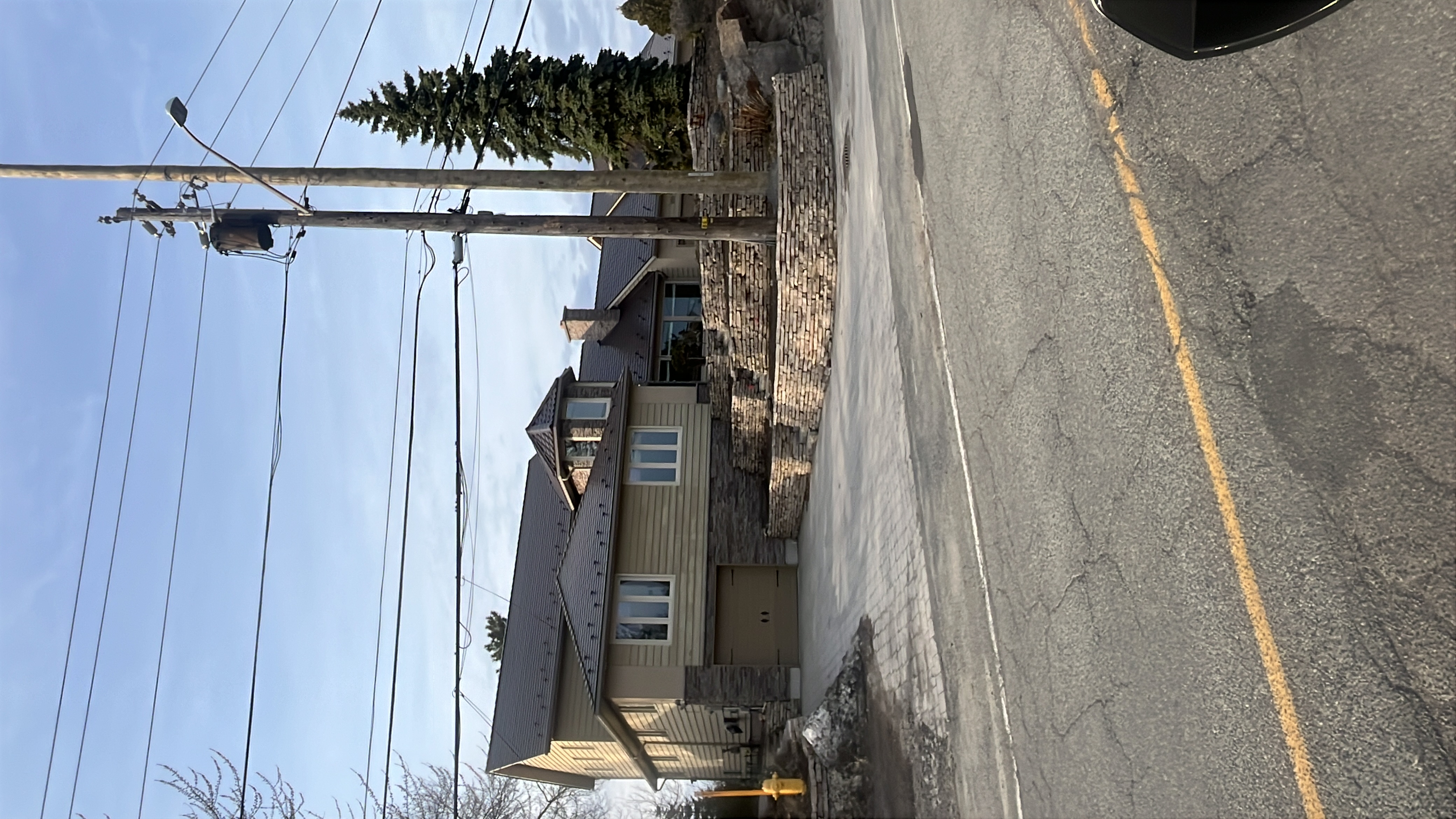 Two-storey craftsman home in Sudbury ON with Interlock Colonial Brown slate metal roofing, multi-hip complex roof, stone retaining walls, and turret feature.