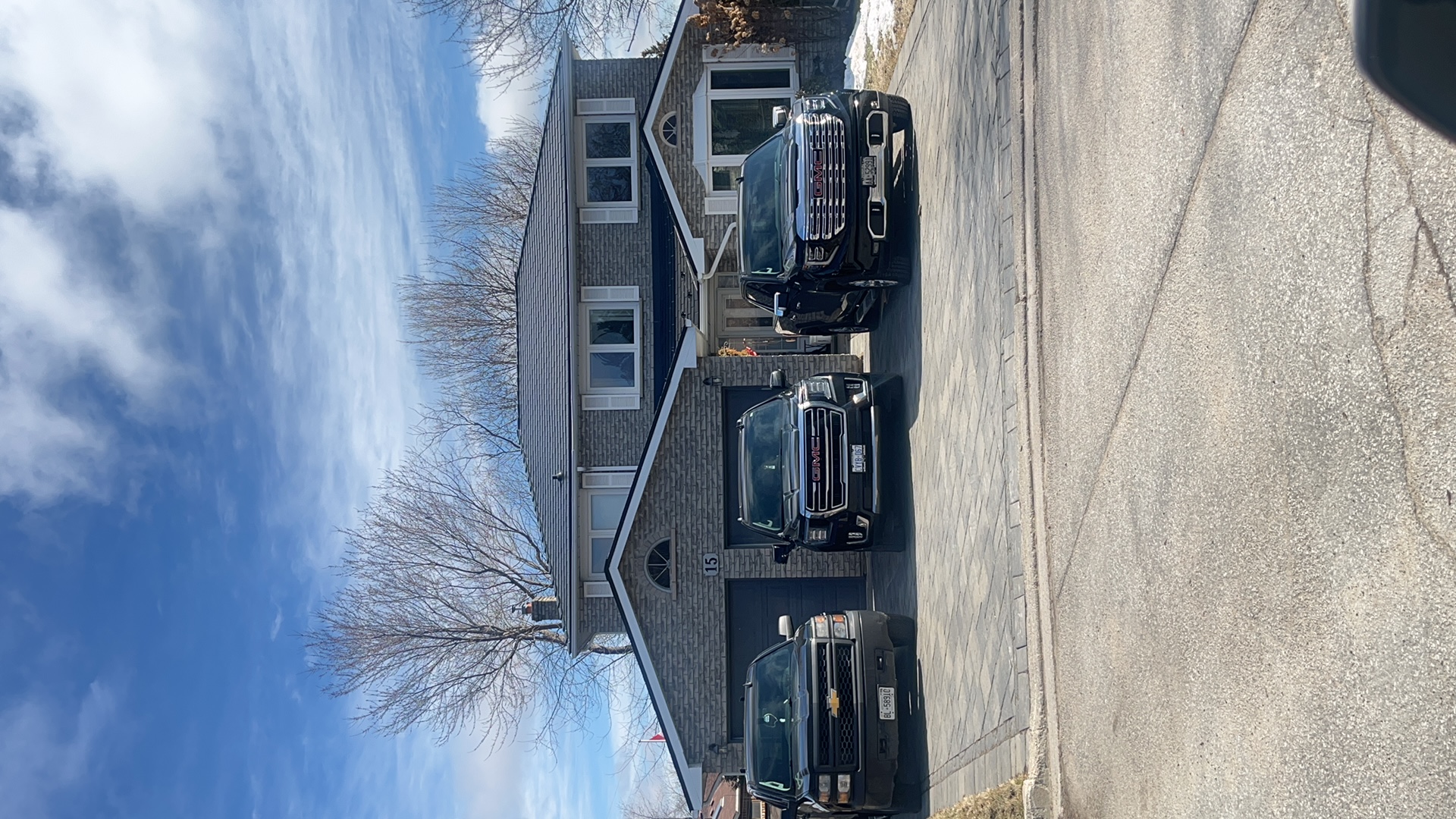 Two-storey brick Colonial home in Bradford, ON with black Interlock aluminum slate metal roofing, double garage, and three black trucks in the driveway.
