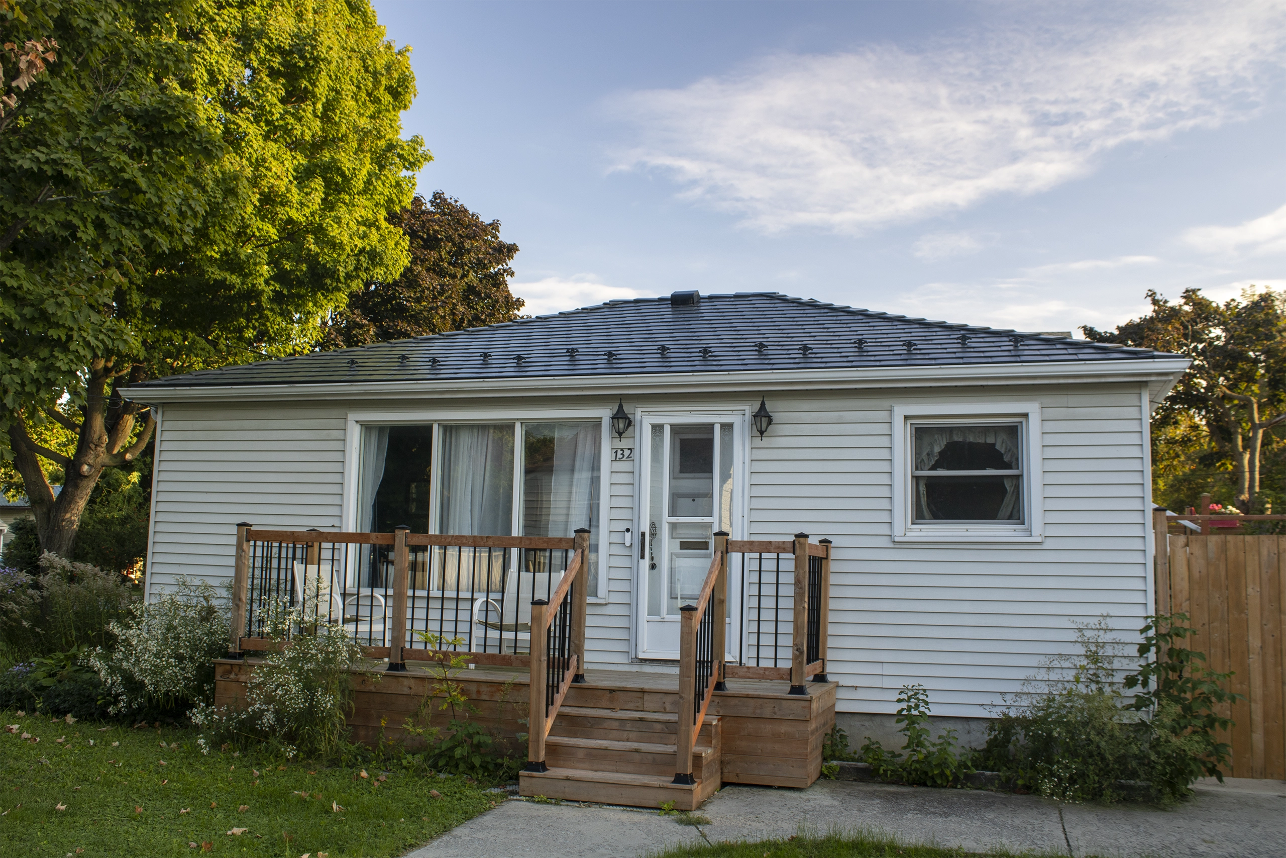 Single-storey ranch-style home in Kingston ON with a low-pitch hip roof clad in deep charcoal Interlock aluminum slate tiles and a new cedar front deck.