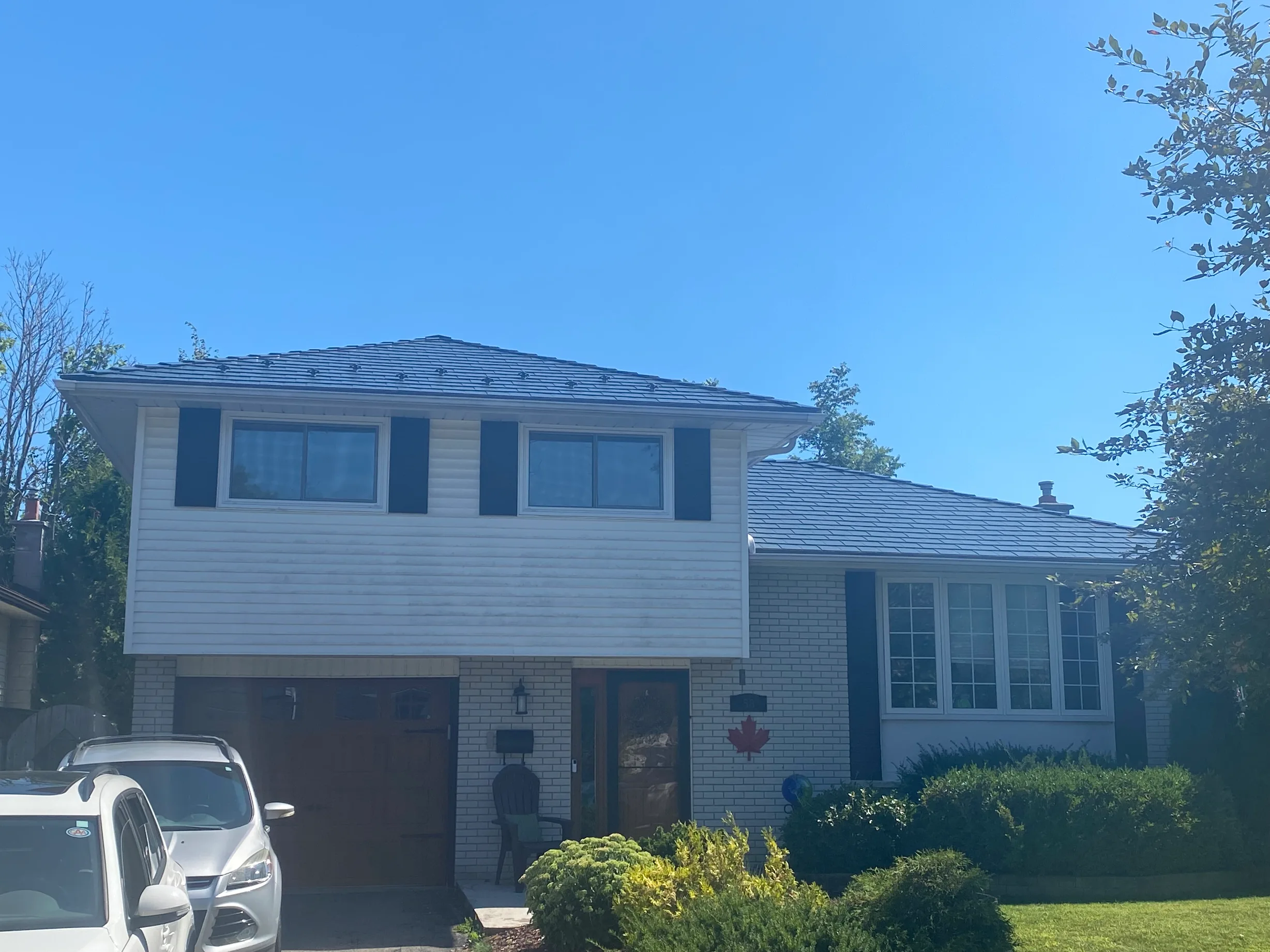 Deep Charcoal Interlock Slate aluminum roof on a white two-storey home with a metal roof among lush, Belleville, Ontario