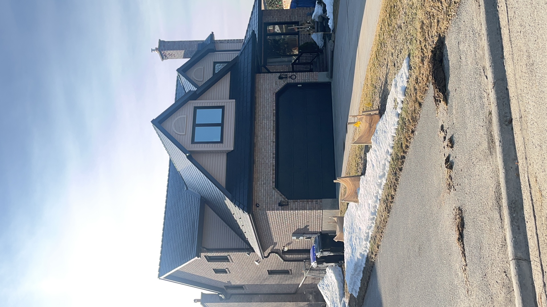 Two-storey Craftsman home in Collingwood ON with black Interlock aluminum slate metal roof, prominent dormer, and brick facade photographed in winter.