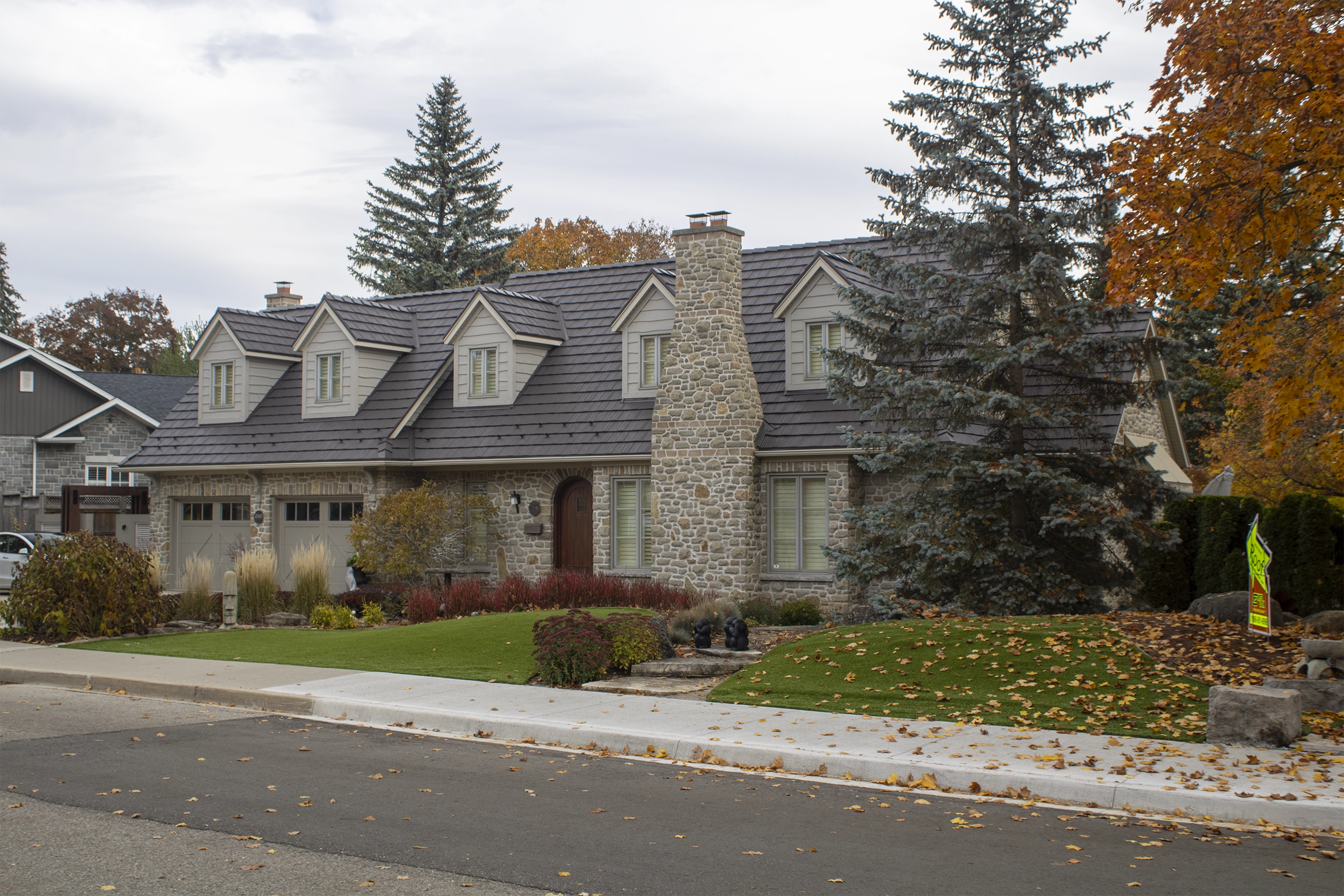 Tudor-style stone home in Waterloo ON with Interlock aluminum shake roofing in Tudor Brown, featuring multiple dormers and a prominent stone chimney.