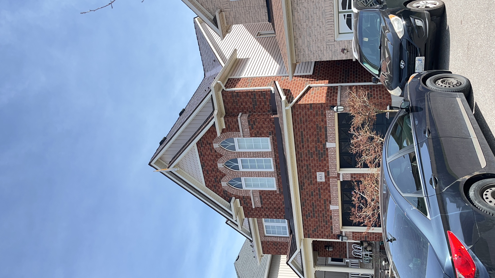 Two-storey red brick Colonial home in Oshawa with Interlock aluminum slate roof in Colonial Brown, featuring steep complex gables and arched upper windows.
