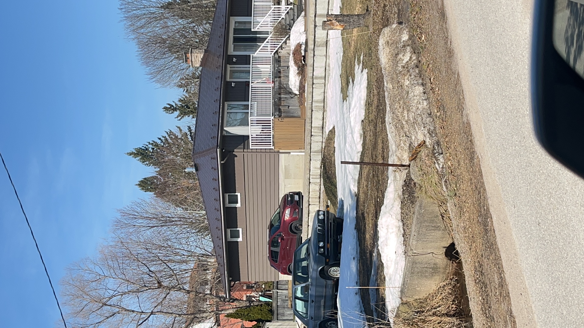 Single-storey ranch home with Interlock Colonial Brown aluminum slate metal roof on a hip profile, chimney visible, photographed in early spring.