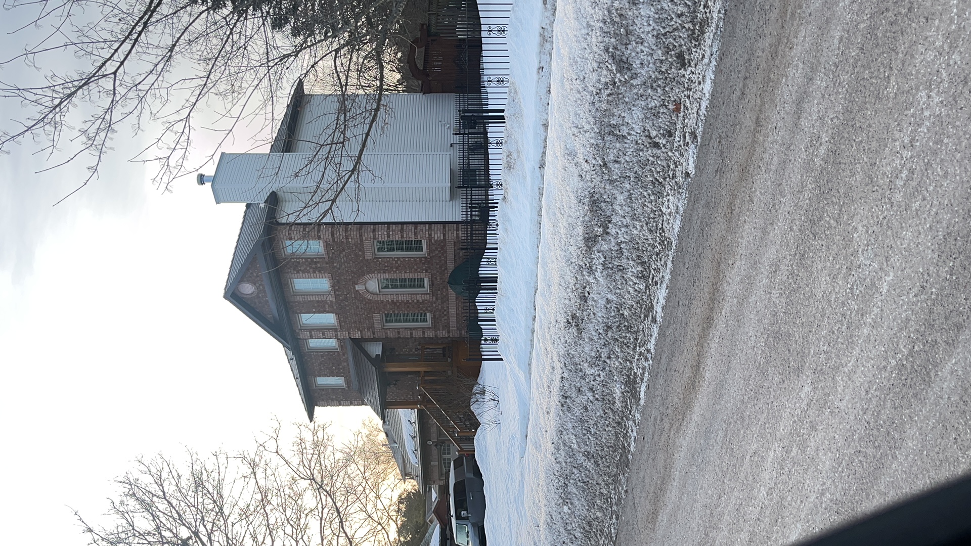 Two-storey brick Colonial home in Angus ON with Interlock Colonial Brown slate metal roof, tall chimney, and iron fence, photographed from street in winter.