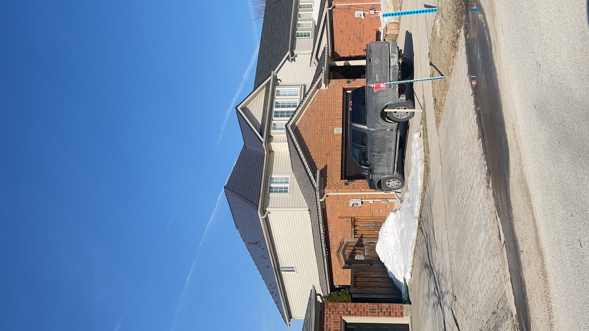 Two-storey brick home in Collingwood, ON with a complex hip roof clad in Interlock Tudor Brown aluminum slate roofing under a clear blue winter sky.