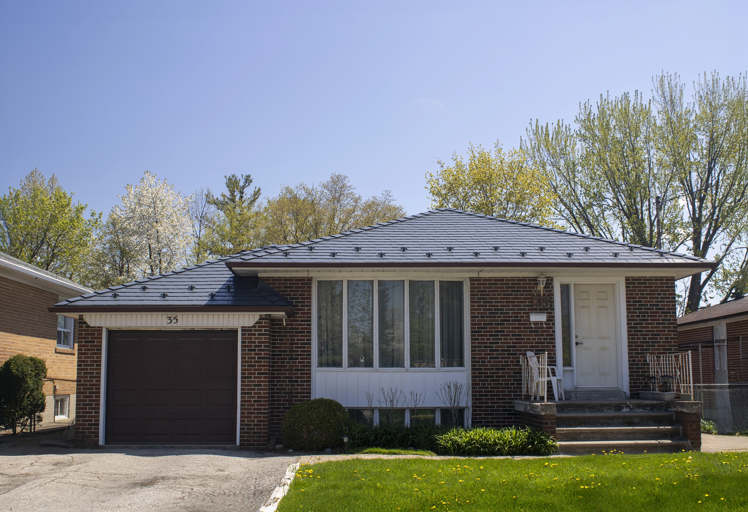 Ranch-style brick bungalow in North York with a deep charcoal Interlock aluminum slate hip roof, single garage, and front entry steps.
