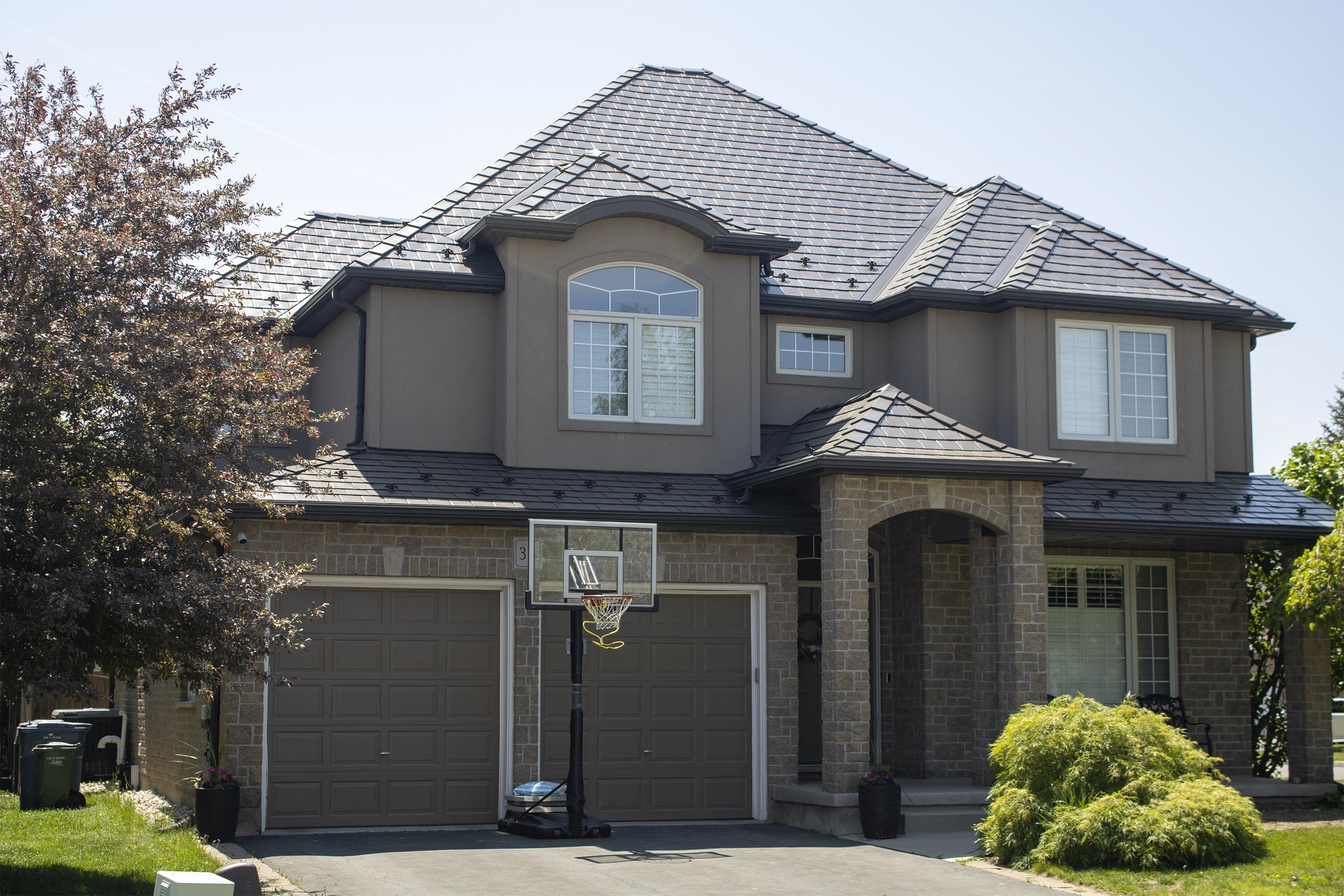 Two-storey suburban home in Guelph ON with complex multi-hip Interlock Tudor Brown aluminum slate metal roofing featuring a central dormer and stone facade.